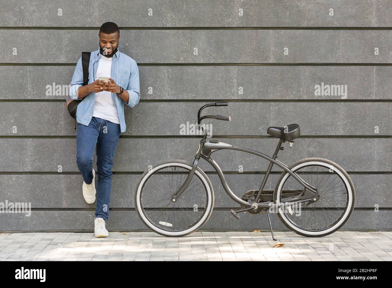 Junger Schwarzer Mann Mit Smartphone, Neben Seinem Fahrrad Im Freien Stehend Stockfoto