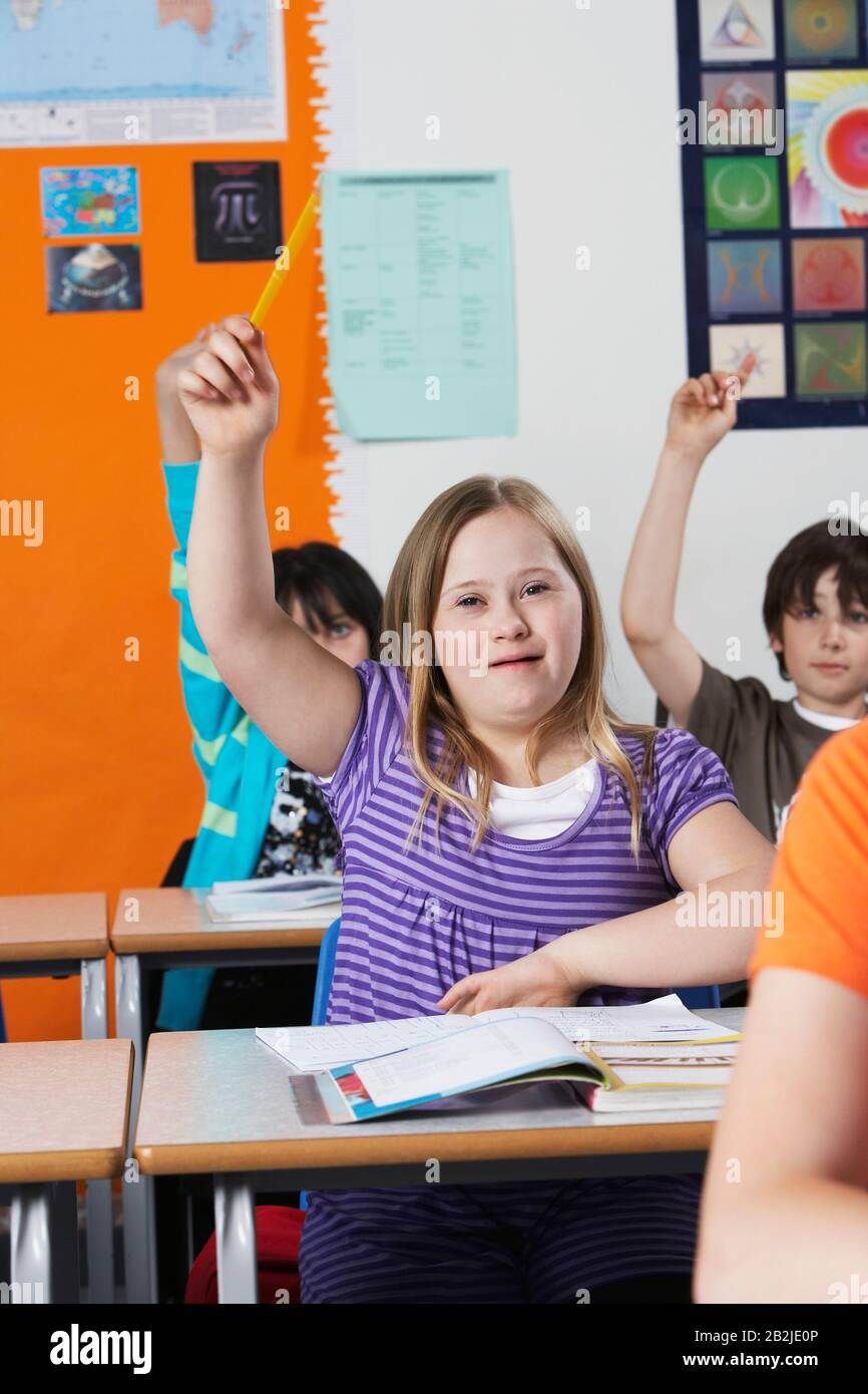 Mädchen (10-12) mit Down-Syndrom, das die Hand im Klassenzimmer erhöht Stockfoto
