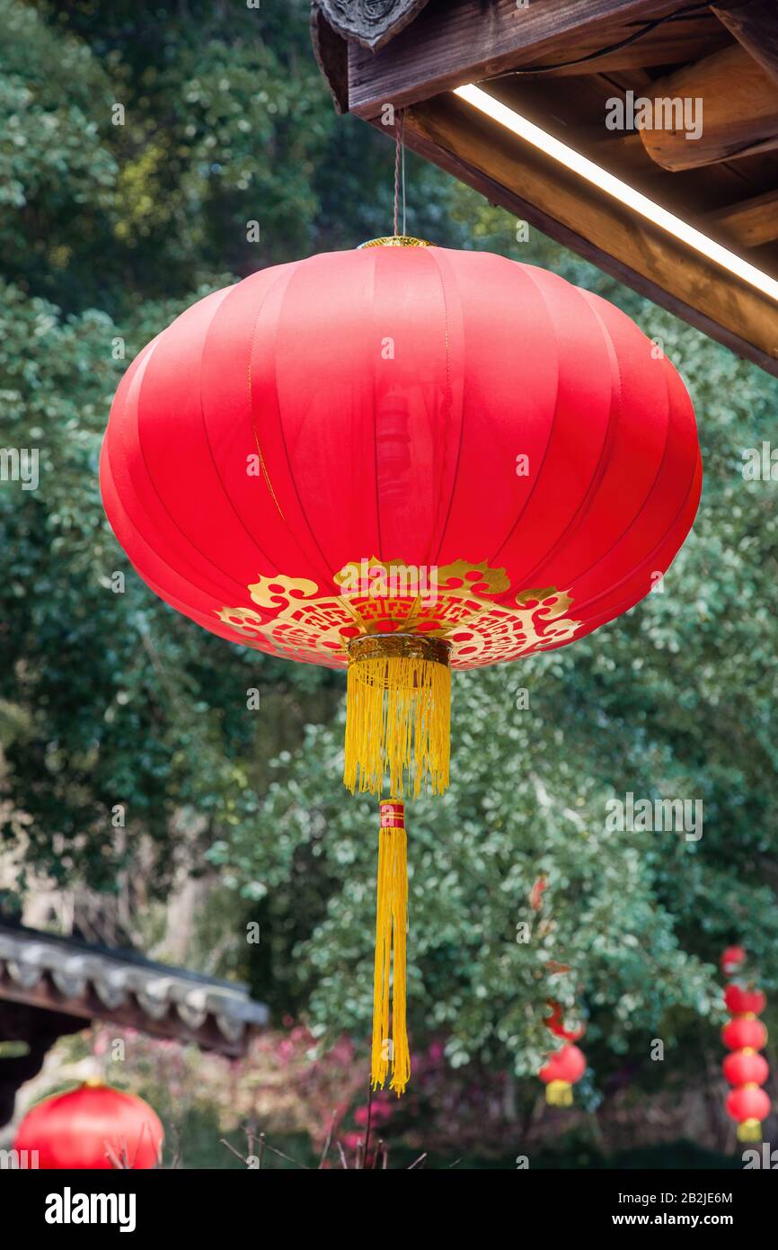 Schöne rote chinesische Laterne, die an Traufen des traditionellen chinesischen alten Holzgebäudes hängt, um den chinesischen Festtag in einem Park zu schmücken, Thr Stockfoto