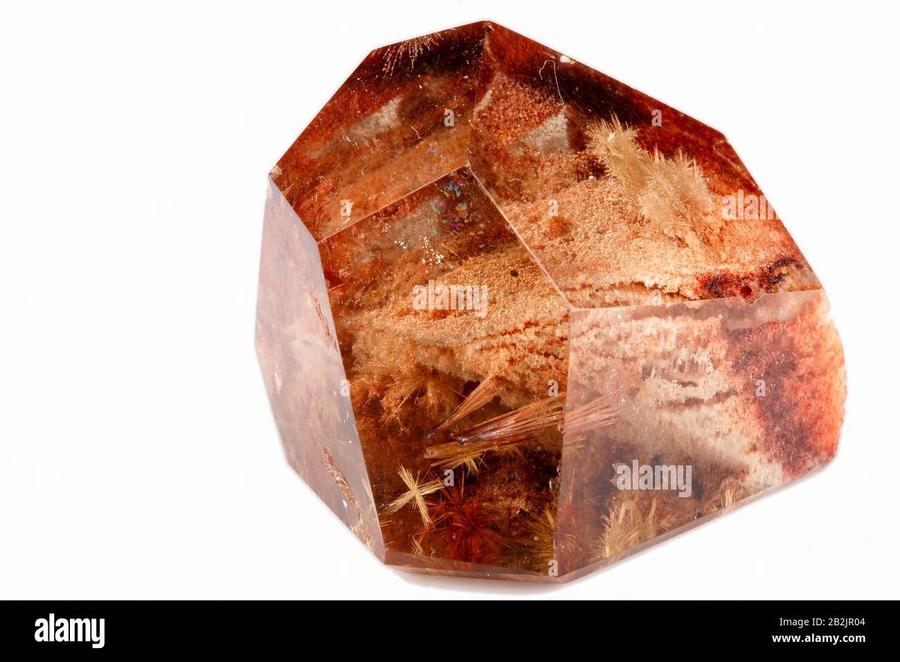 Ein einzelner, facettierter, durchscheinender brauner Kristall mit geometrischer, facettierter Form. Der Kristall enthält zahlreiche innere Fasereinschlüsse, von denen einige als feine, haarartige Strukturen und andere erscheinen Stockfoto