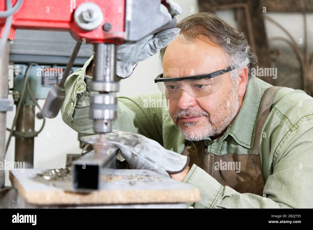 Reifer Mann, der während der Arbeit mit Maschinen in der Werkstatt Schutzbrille trägt Stockfoto