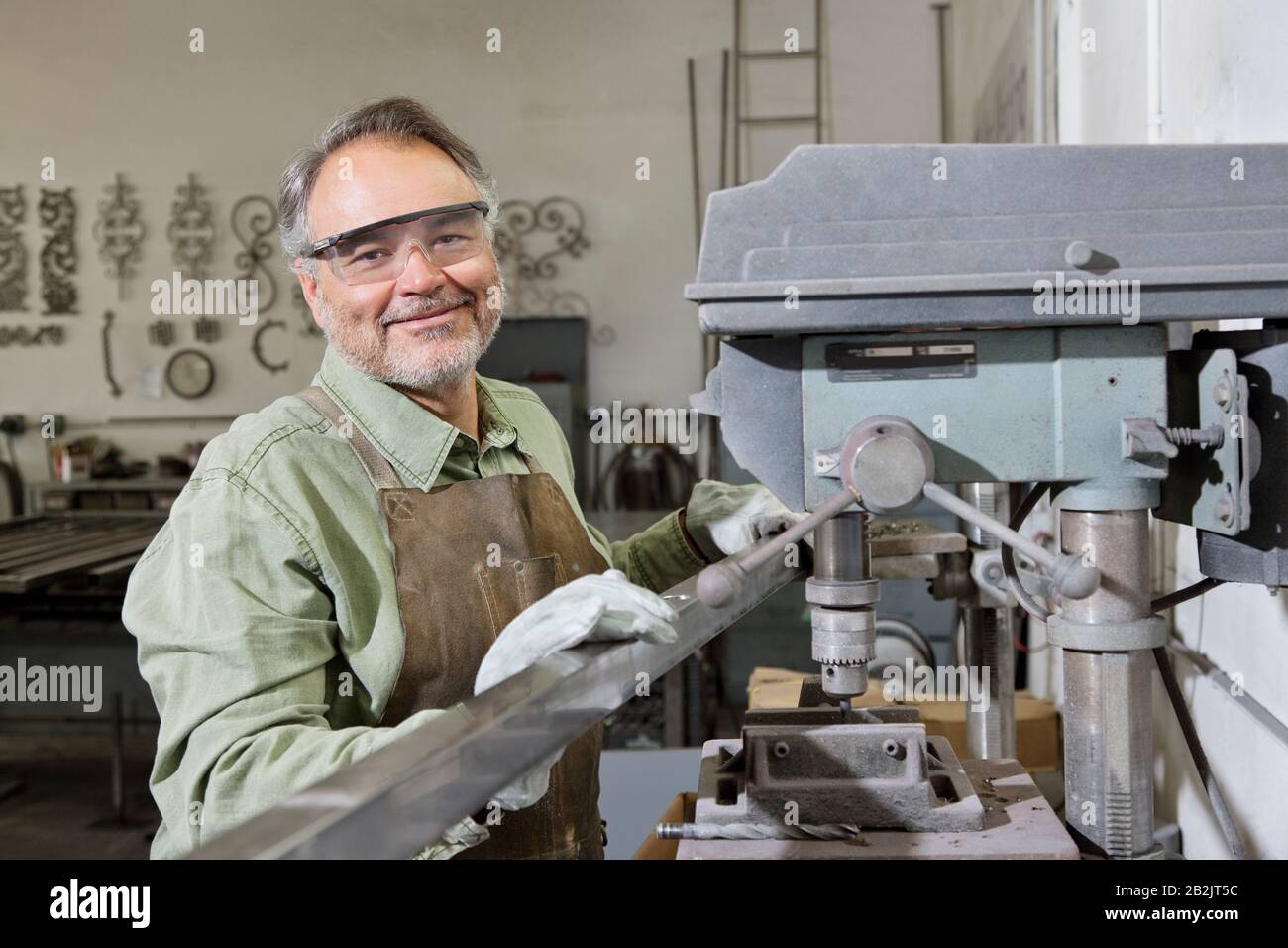 Portrait eines glücklichen, reifen Mannes, der eine Schutzbrille trägt, die an Maschinen in der Werkstatt steht Stockfoto