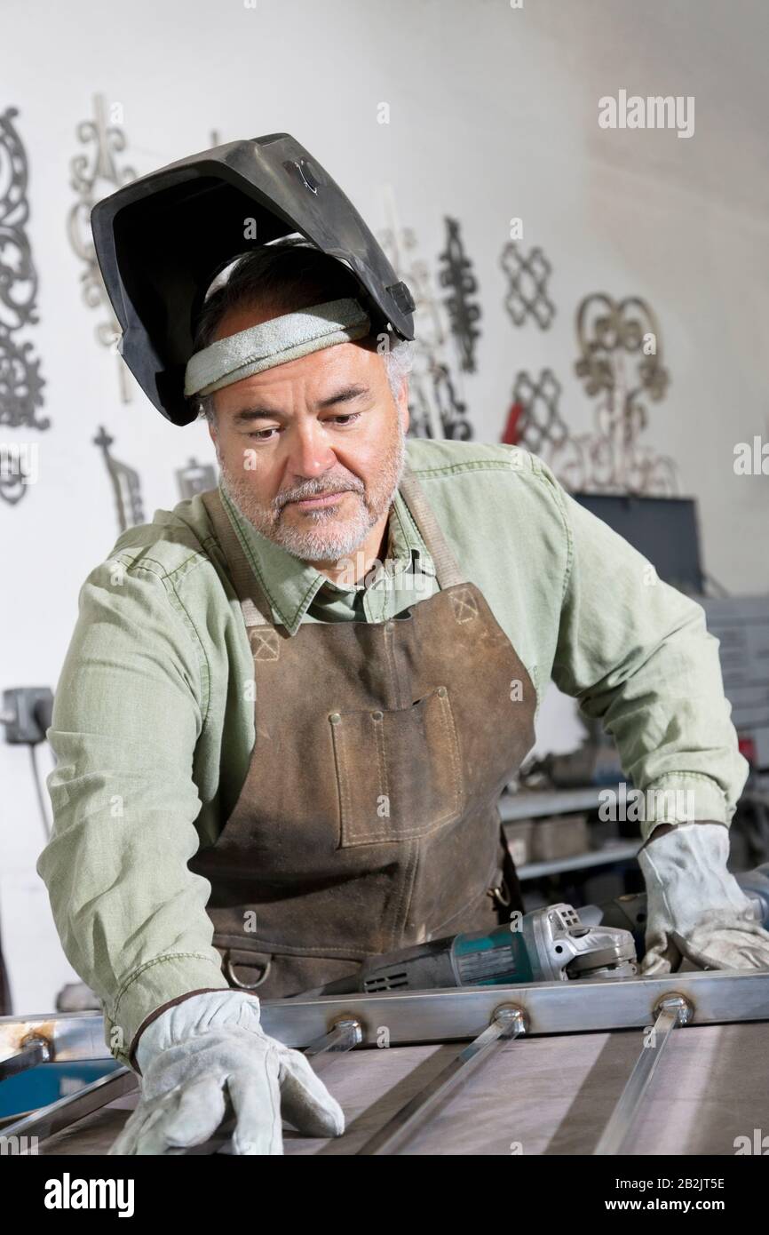 Reifer Mann trägt Schutzmaske und arbeitet in der Werkstatt an Metall Stockfoto