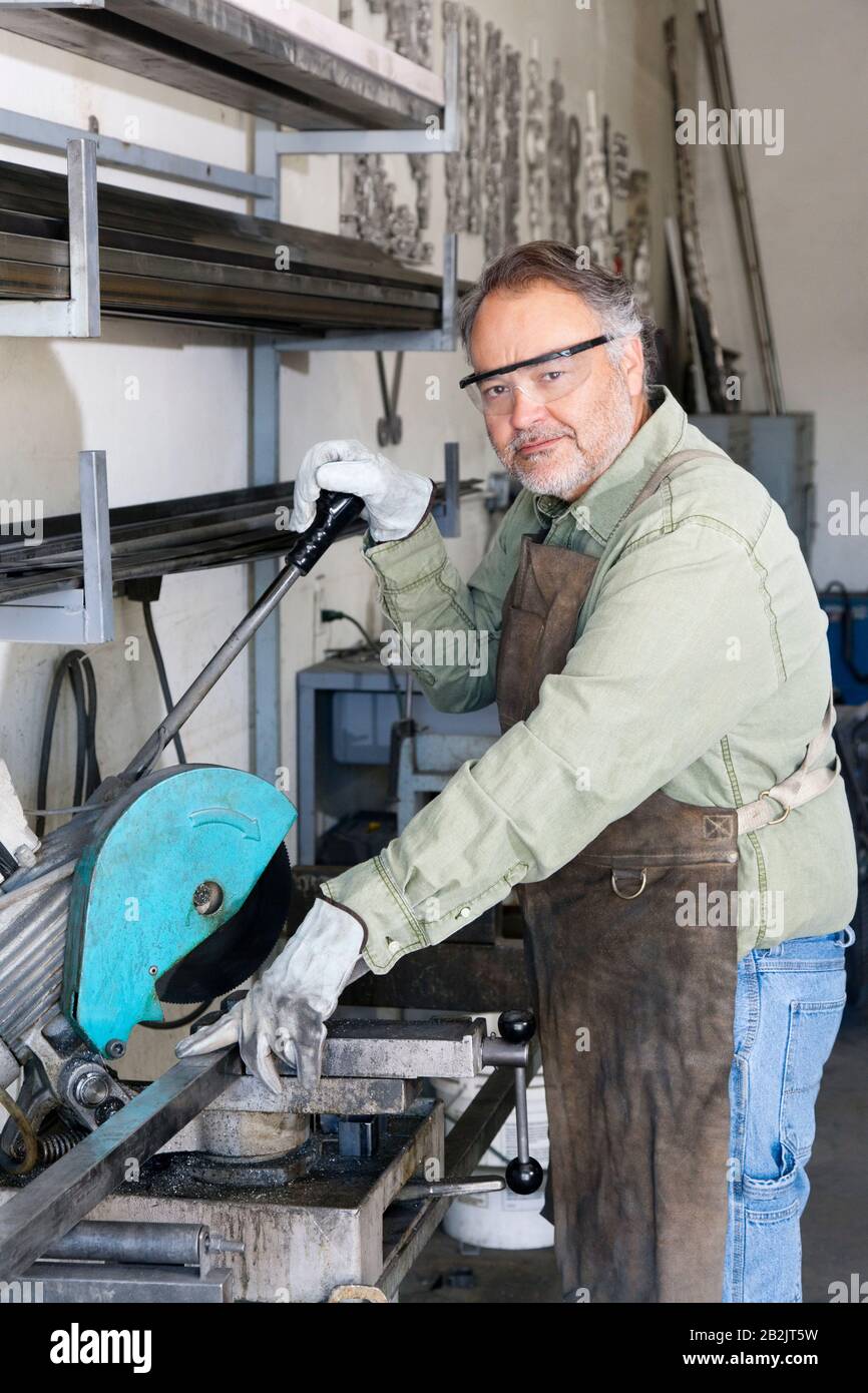 Porträt eines reifen Metallarbeiters, der in der Werkstatt mit Elektrosäge arbeitet Stockfoto
