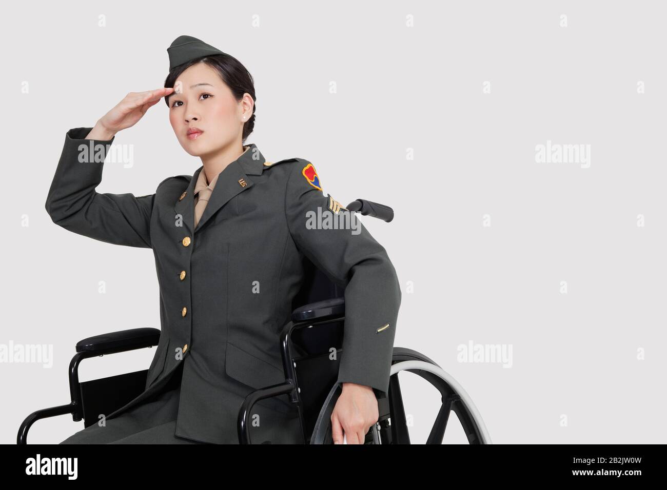 US-Militäroffizierin im Rollstuhl, die über grauen Hintergrund saluiert Stockfoto