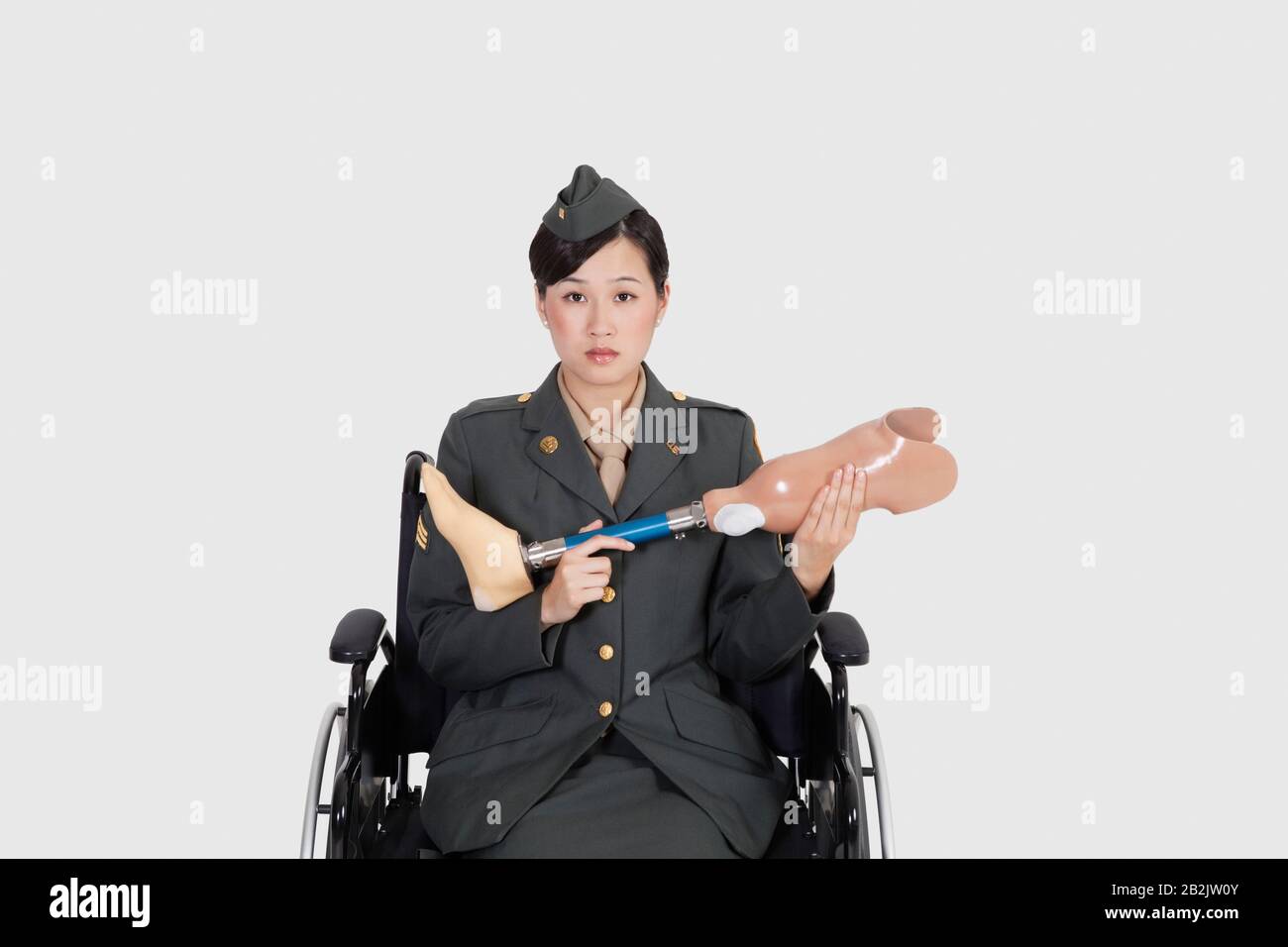 US-Militäroffizier im Rollstuhl, der künstliche Extremitäten über grauen Hintergründen hält Stockfoto