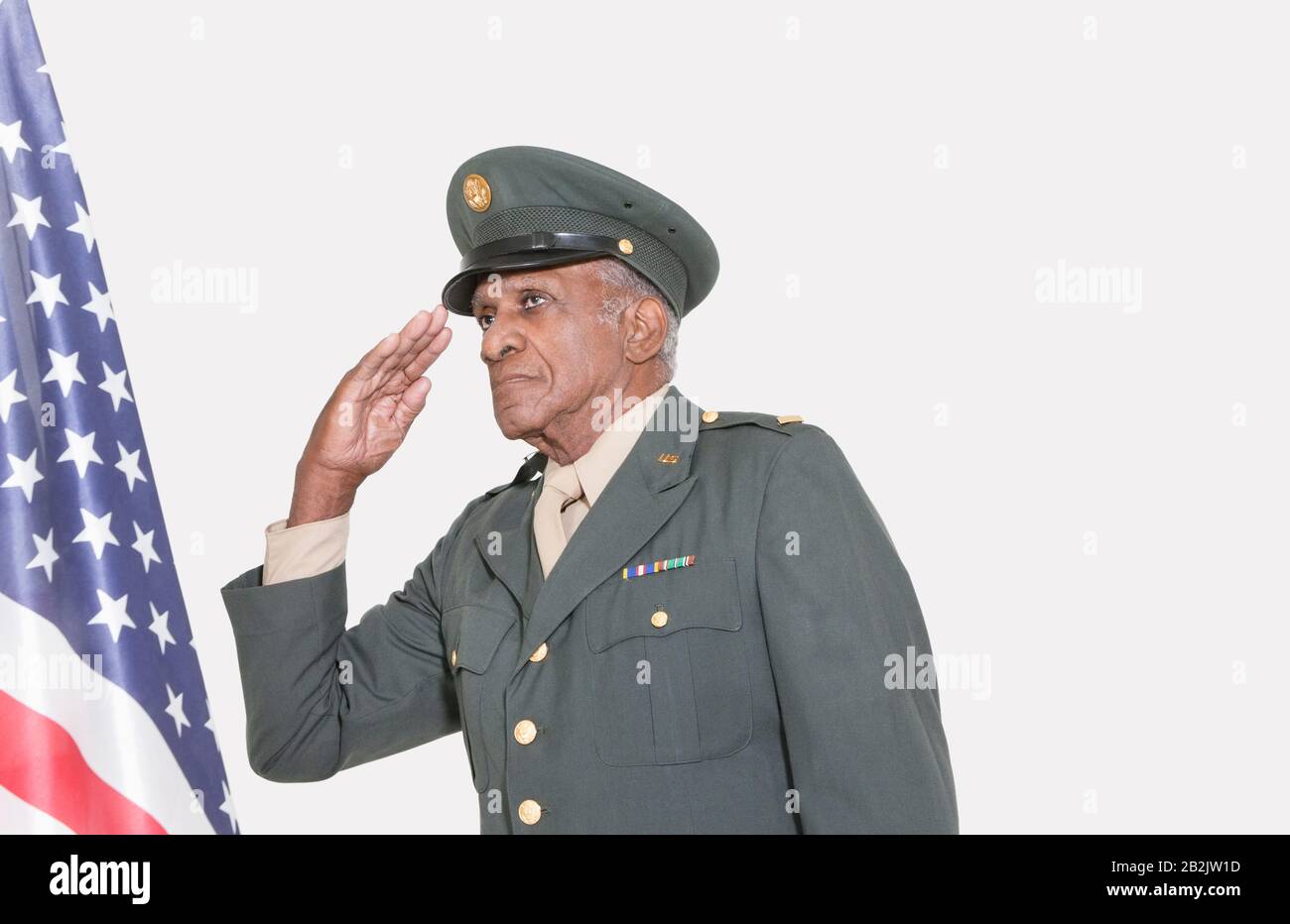 Hoher männlicher US-Militäroffizier, der die amerikanische Flagge über grauem Hintergrund salutieren soll Stockfoto
