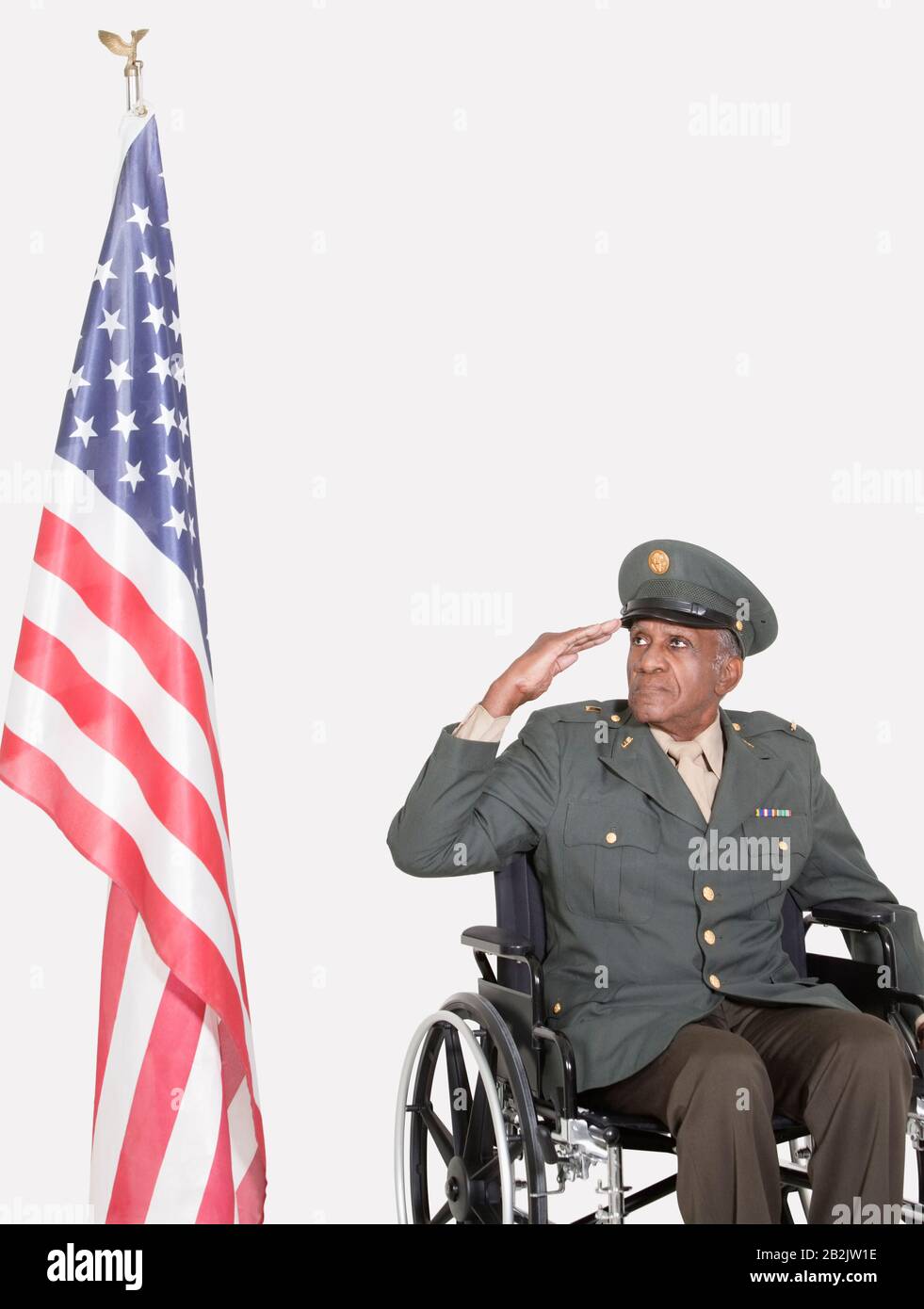 Ranghoher männlicher US-Militäroffizier im Rollstuhl, die amerikanische Flagge über grauem Hintergrund salutieren Stockfoto