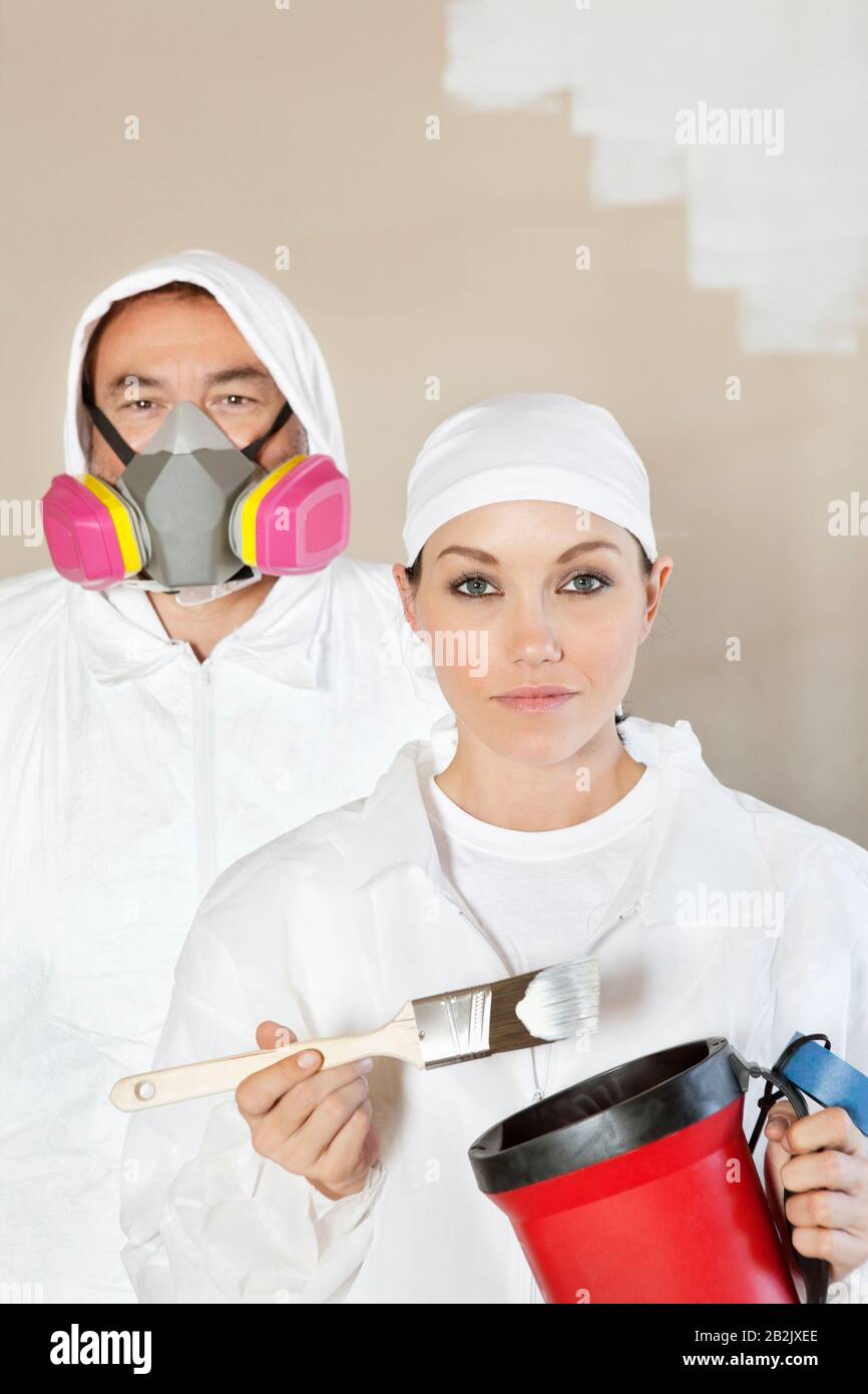 Porträt der Arbeiterinnen, die Farbwerkzeuge mit einem männlichen Arbeiter im Hintergrund halten Stockfoto