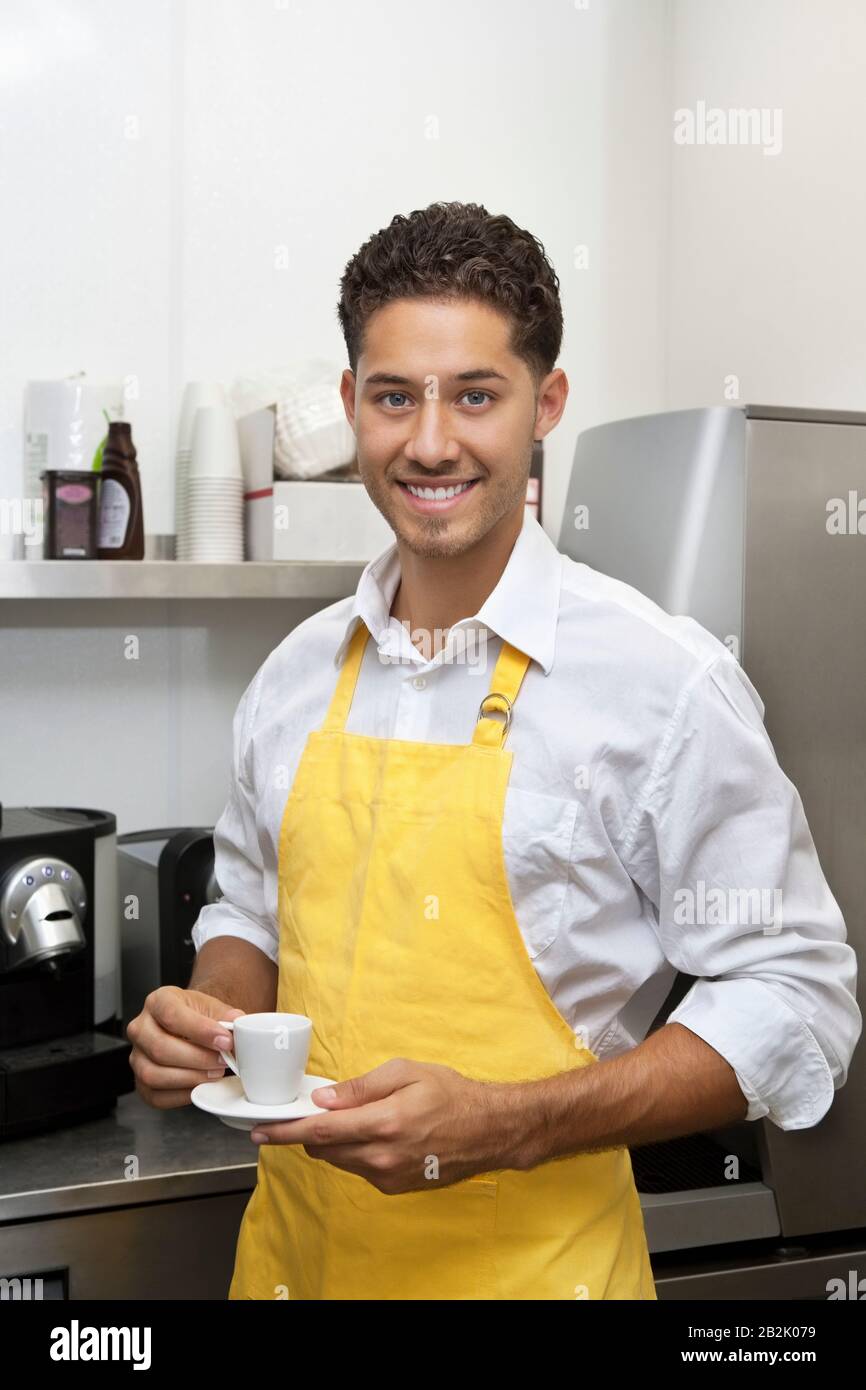 Porträt des jungen männlichen Kellners, der Tasse und Untertasse hält Stockfoto