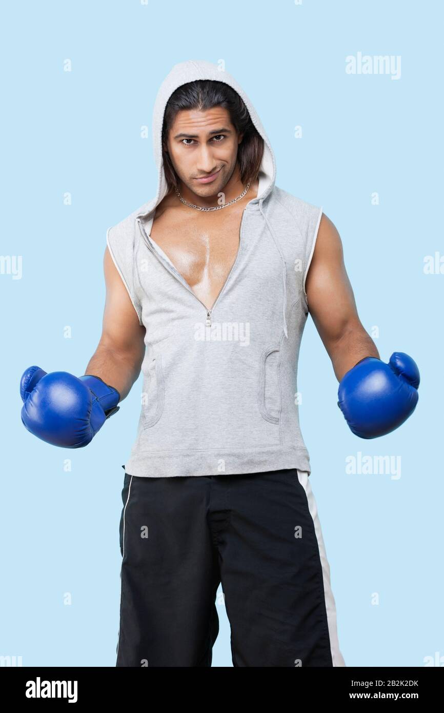 Porträt eines selbstbewussten jungen Mannes, der Boxhandschuhe trägt, die über blauem Hintergrund stehen Stockfoto
