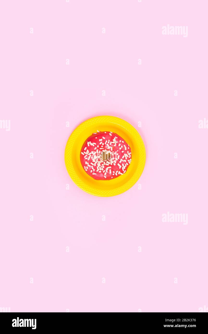 Pinkfarbener Donut auf gelber Platte auf pinkfarbenem Hintergrund. Zucker und Fettleibigkeit. Abstraktion und Minimalismus. Stockfoto