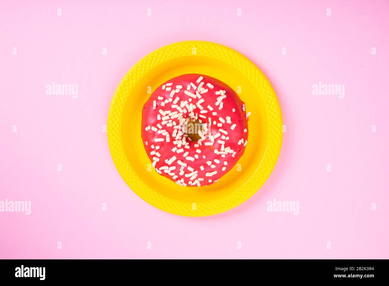 Pinkfarbener Donut auf gelber Platte auf pinkfarbenem Hintergrund. Zucker und Fettleibigkeit. Abstraktion und Minimalismus. Stockfoto