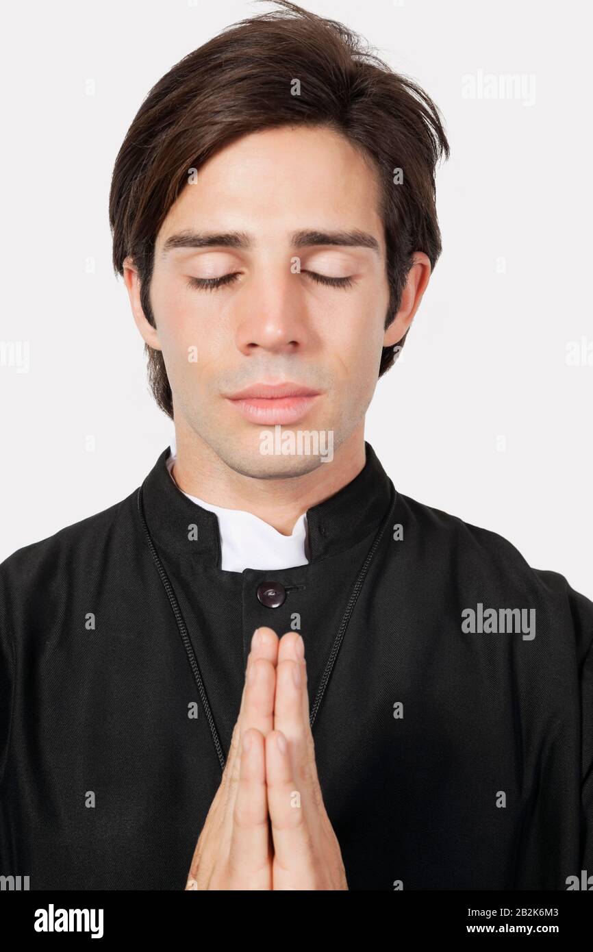 Junger Mann im Kostüm des Priesters, der vor grauem Hintergrund betet Stockfoto