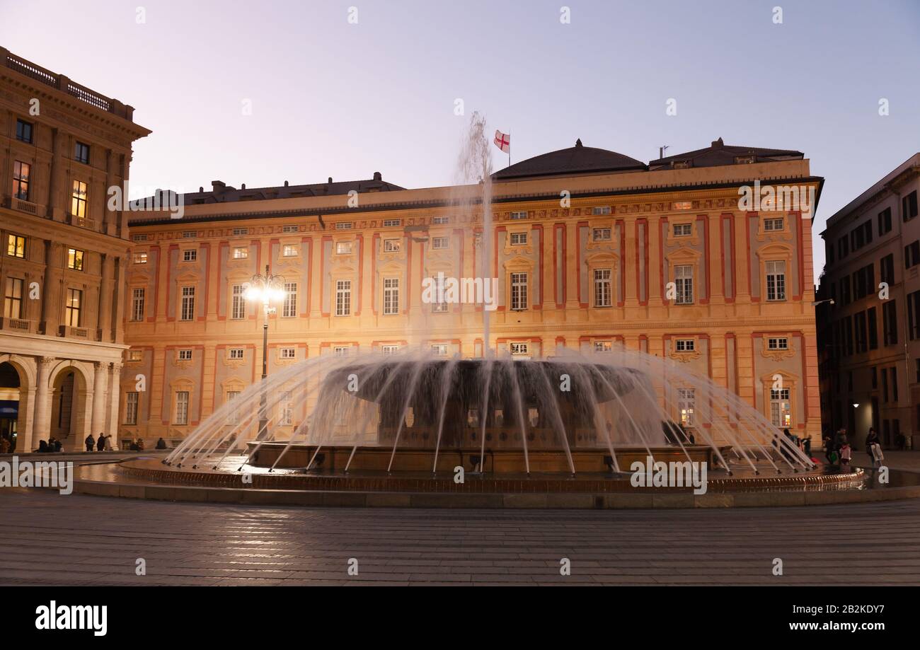Nachtblick auf den Brunnen an der Piazza De Ferrari in Genova, normale, nicht erkennbare Menschen gehen die Straße Stockfoto