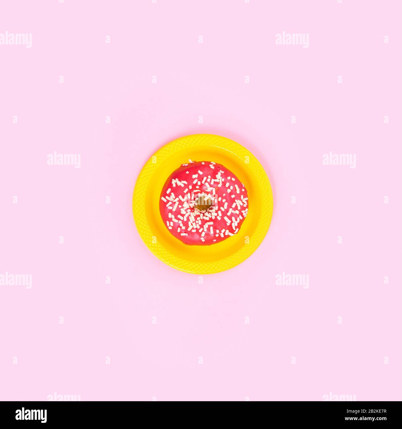 Pinkfarbener Donut auf gelber Platte auf pinkfarbenem Hintergrund. Zucker und Fettleibigkeit. Abstraktion und Minimalismus. Stockfoto