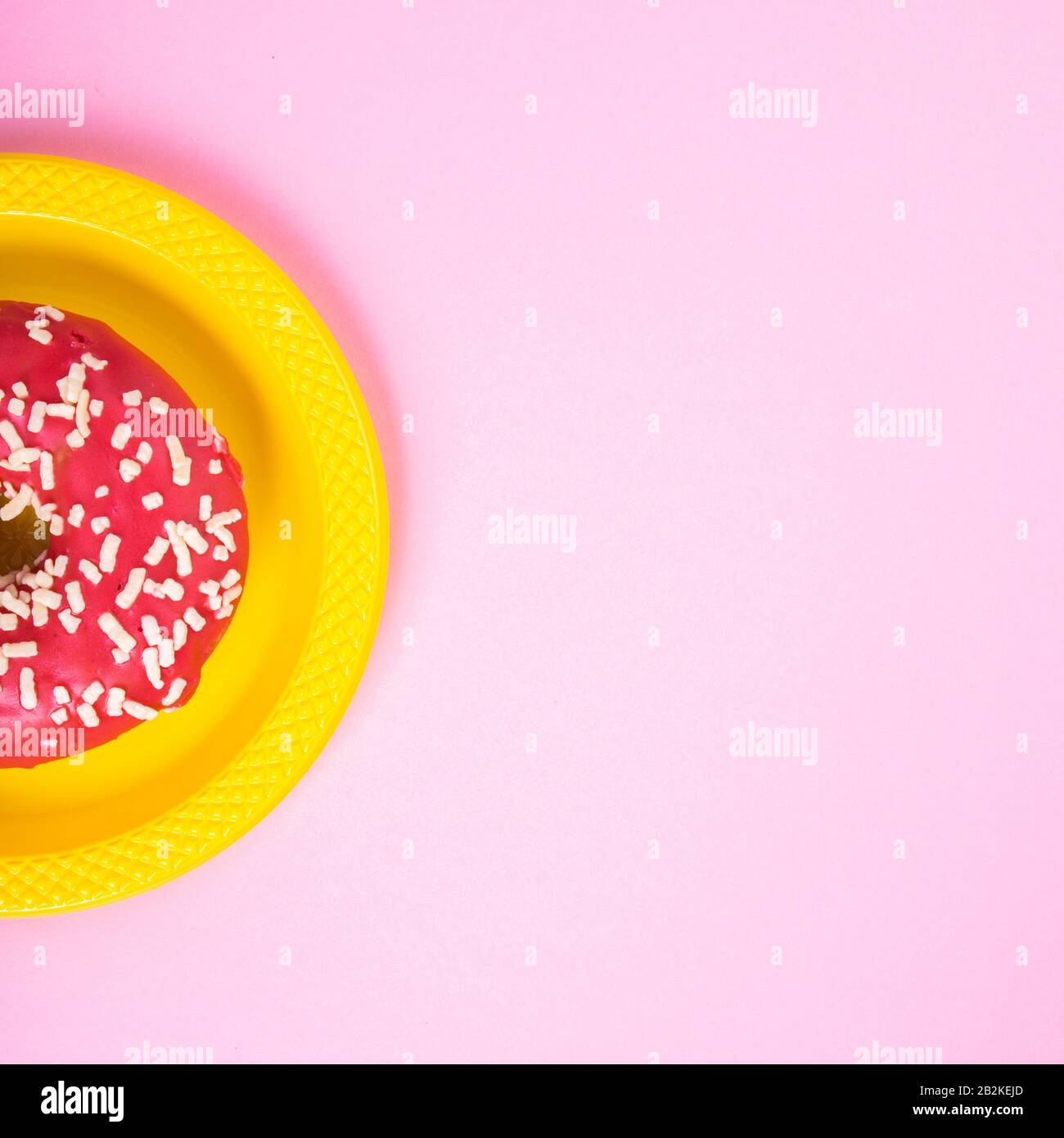 Pinkfarbener Donut auf gelber Platte auf pinkfarbenem Hintergrund. Zucker und Fettleibigkeit. Abstraktion und Minimalismus. Stockfoto
