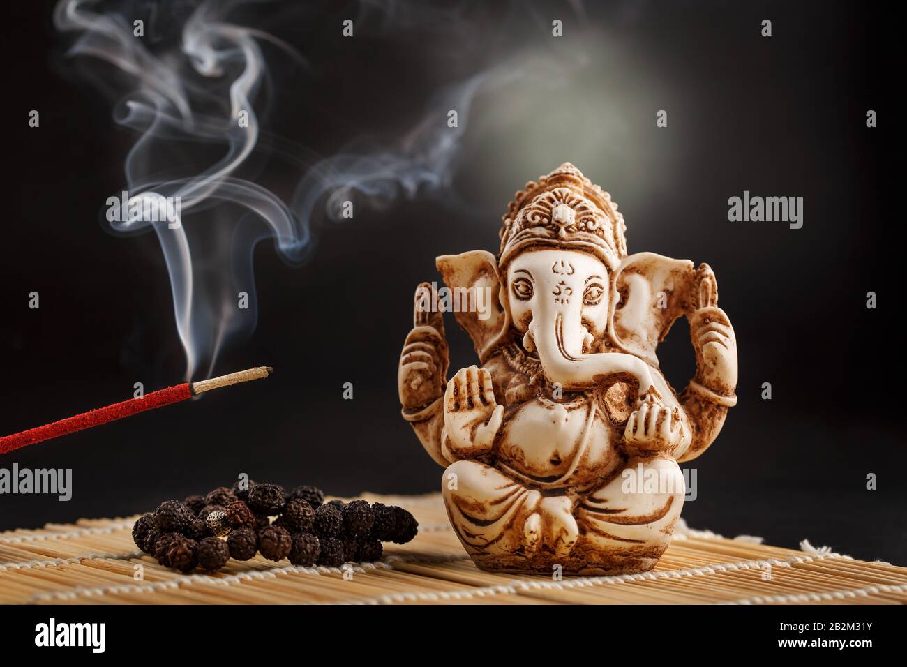 hindu-gott Ganesh auf schwarzem Grund. Rudraksha-Statue und Rosar auf einem Holztisch mit rotem Räucherstäbchen und Räucherstrauch. Kopierbereich Stockfoto