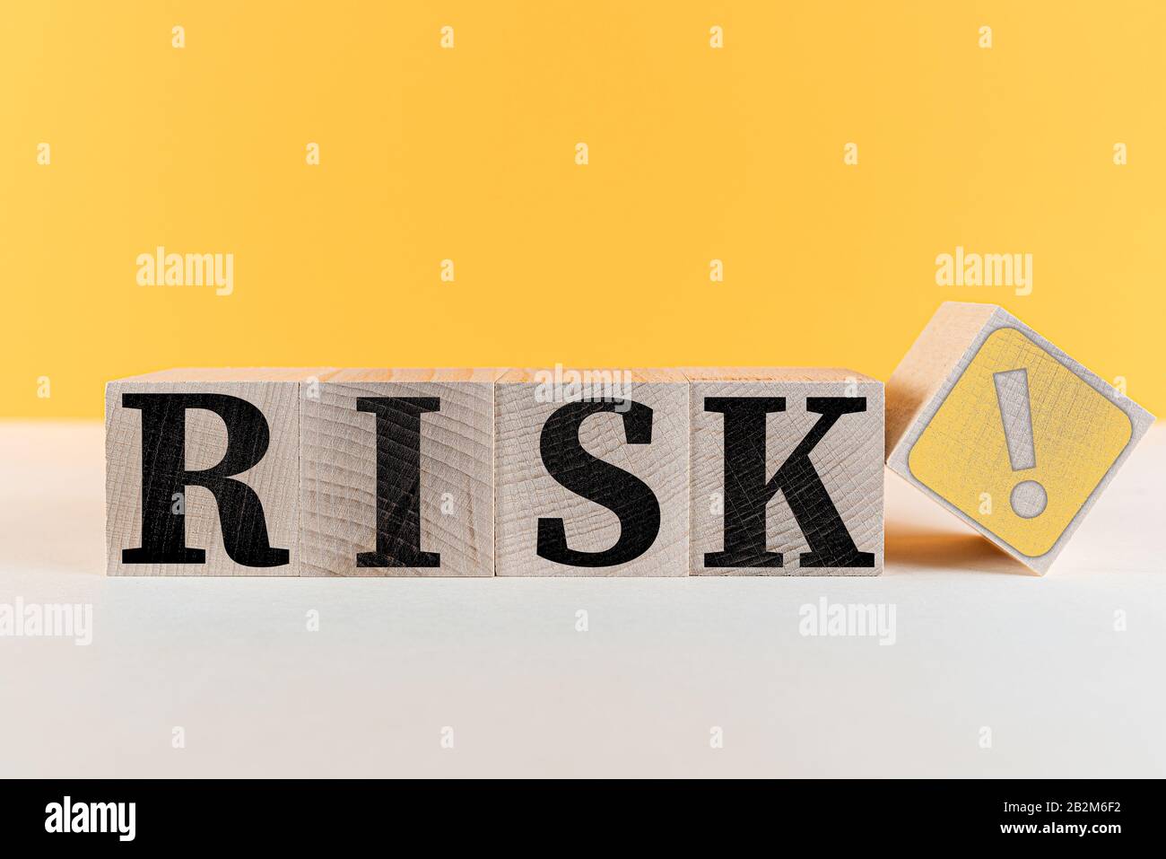 WORTRISIKO und Risikosymbol mit Ausrufezeichen auf Holzwürfeln vor orangefarbenem Hintergrund Stockfoto