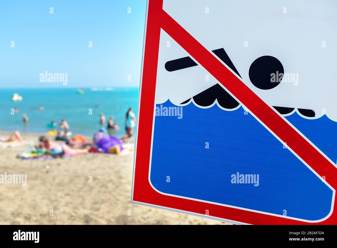 Ein Schild am Strand darf Die Menschen trotz Schild und Verbot nicht baden und sich auf dem Meer ausruhen. Der Begriff Regelverstoß und Stockfoto