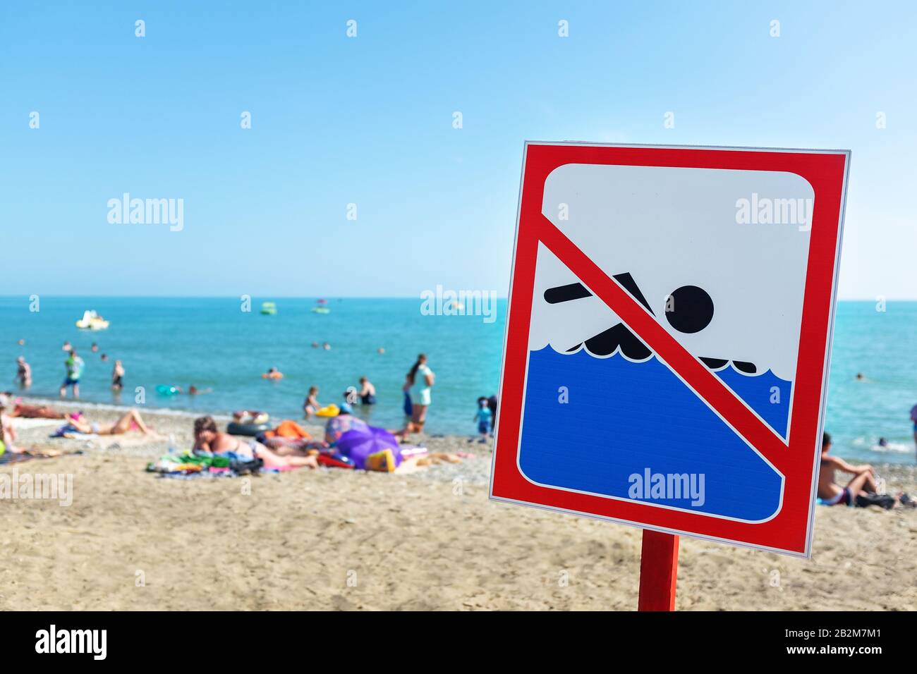 Ein Schild am Strand darf Die Menschen trotz Schild und Verbot nicht baden und sich auf dem Meer ausruhen. Der Begriff Regelverstoß und Stockfoto