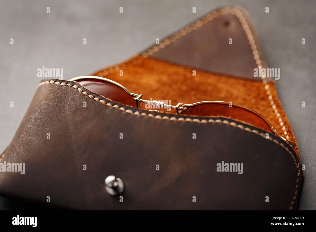 Tasche aus echtem braunem Leder, handgefertigt auf dunklem Hintergrund. Brille im Gehäuse. Nahaufnahme Stockfoto
