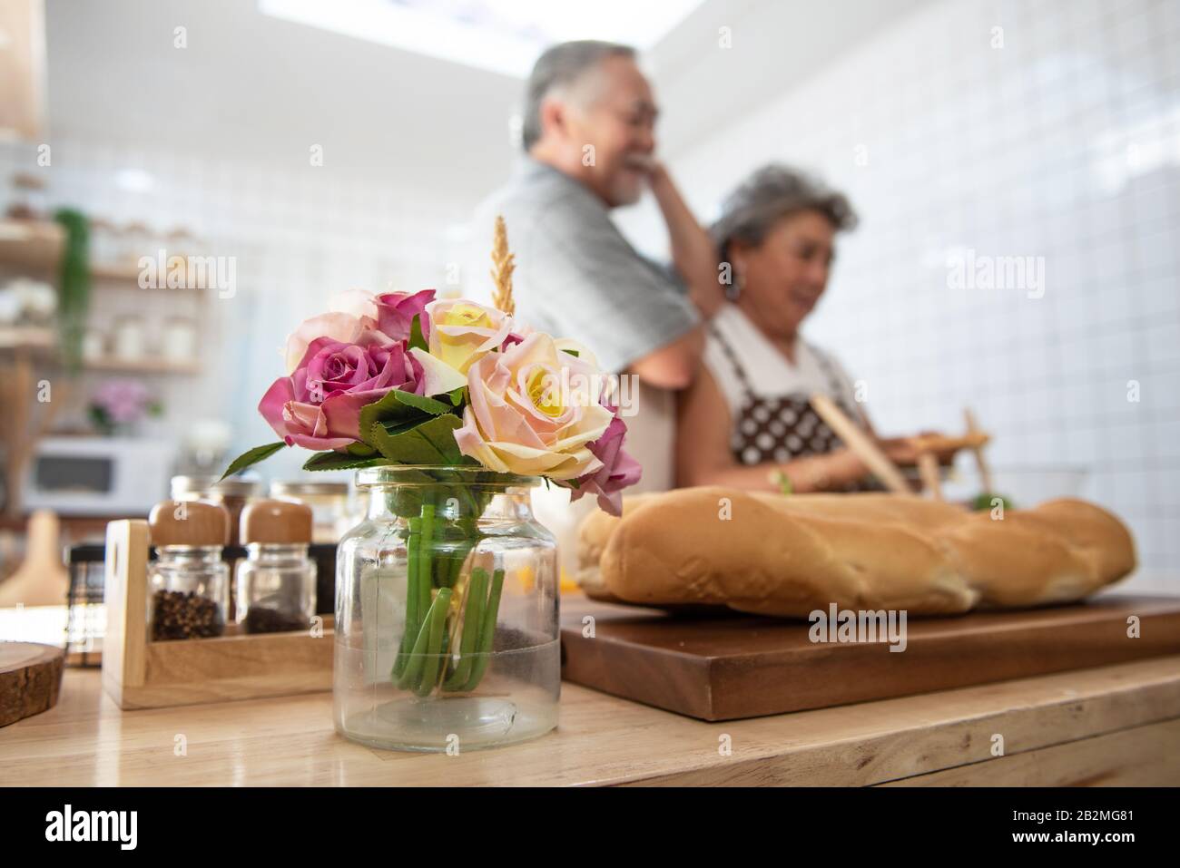 Selektiv konzentriert sich auf Rose auf den Tisch in der Küche mit älterem älterem asiatischem Paar, das Abendessen im Hintergrund kocht.Liebe ist überall und überall. Stockfoto
