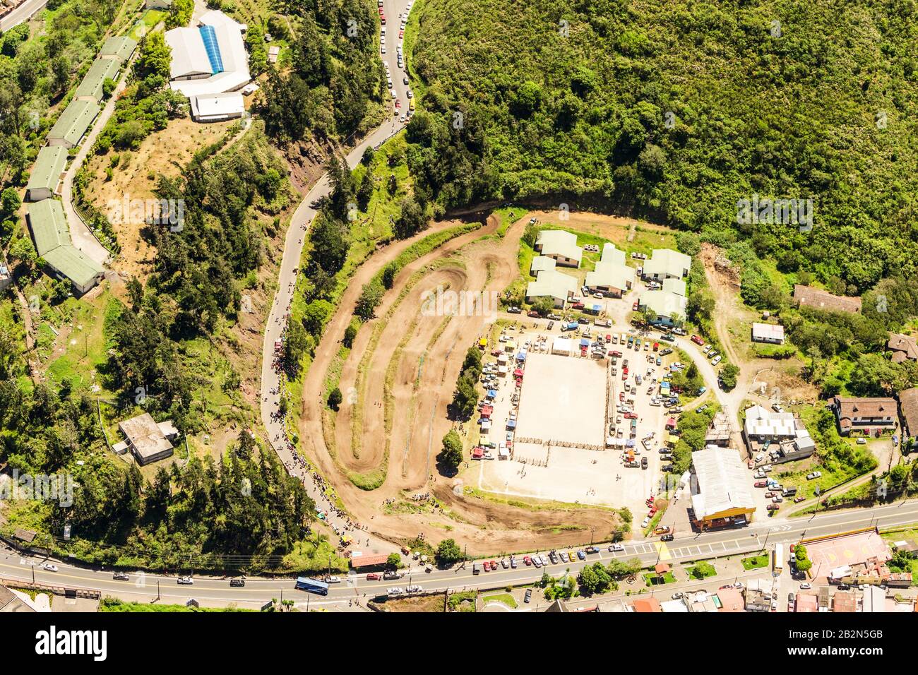 Ein Luftbild zeigt eine Baustelle in einer hügeligen, grünen Landschaft. Das Gelände verfügt über freigelegte Erde mit sichtbaren Reifenspuren, mehrere temporäre Bauten mit hellen Dächern Stockfoto