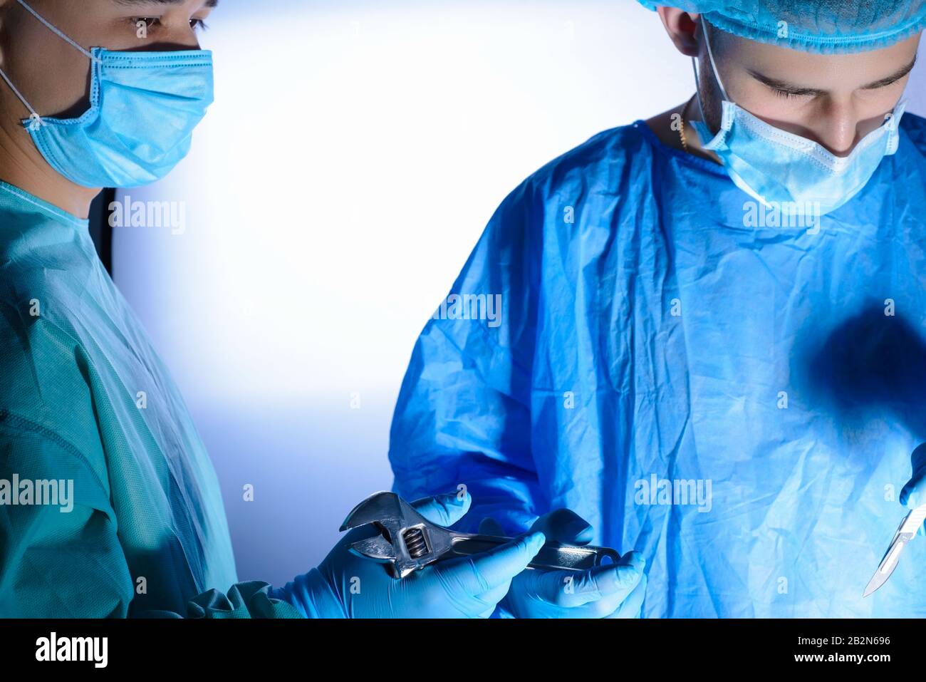 Nahaufnahme, Porträt zweier Chirurgen, in medizinischen Masken und sterilem Gown. Der Assistent gibt den Schlüssel an den Chirurgen weiter. Medizinischer Humor. Chirurgischer Witz. Stockfoto