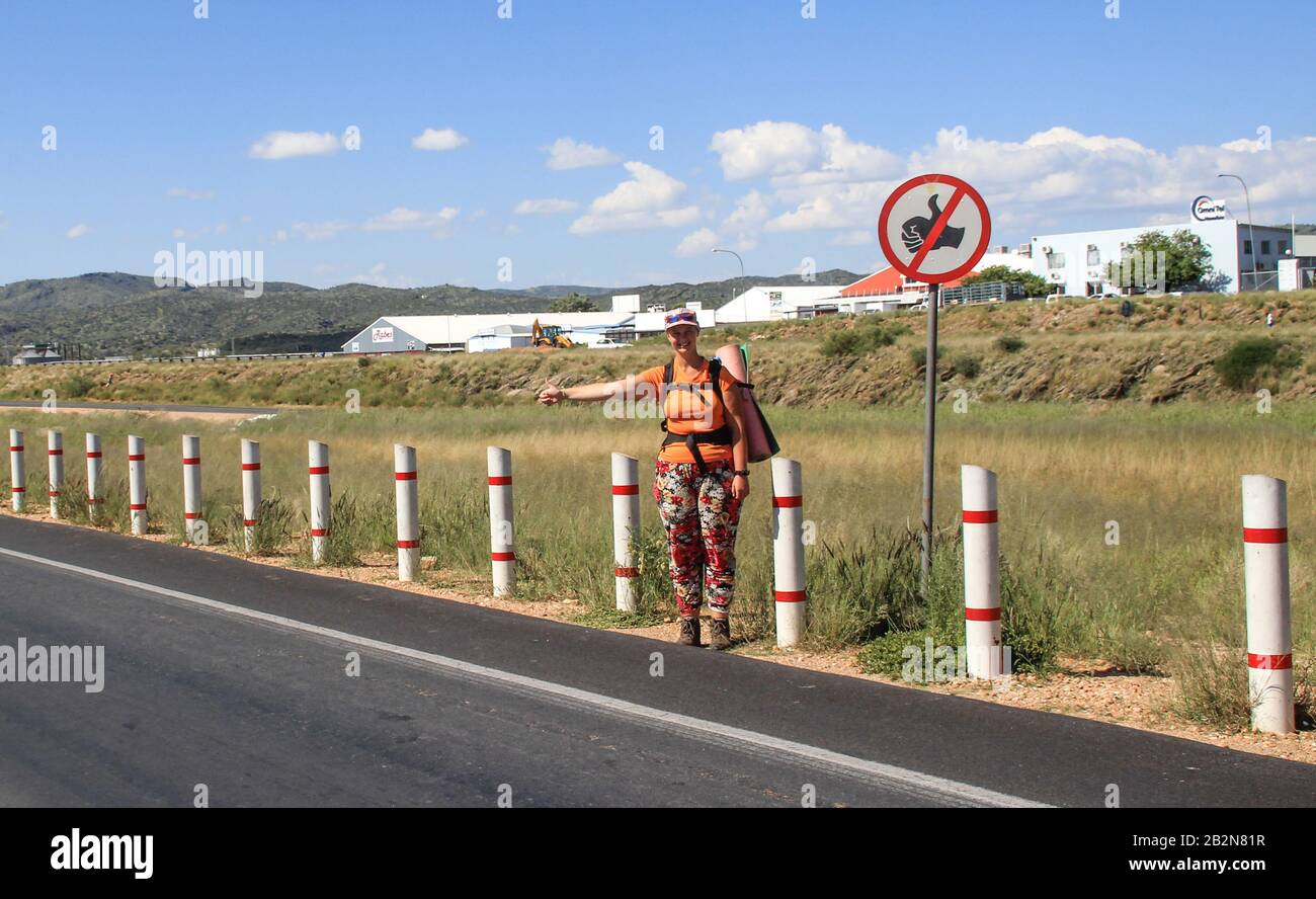 Swakopmund, Namibia - 15. Mai 2015: Junges weißes Touristenmädchen hitchwander und stoppt das Auto unter dem Schild "Hexerei ist verboten". Stockfoto