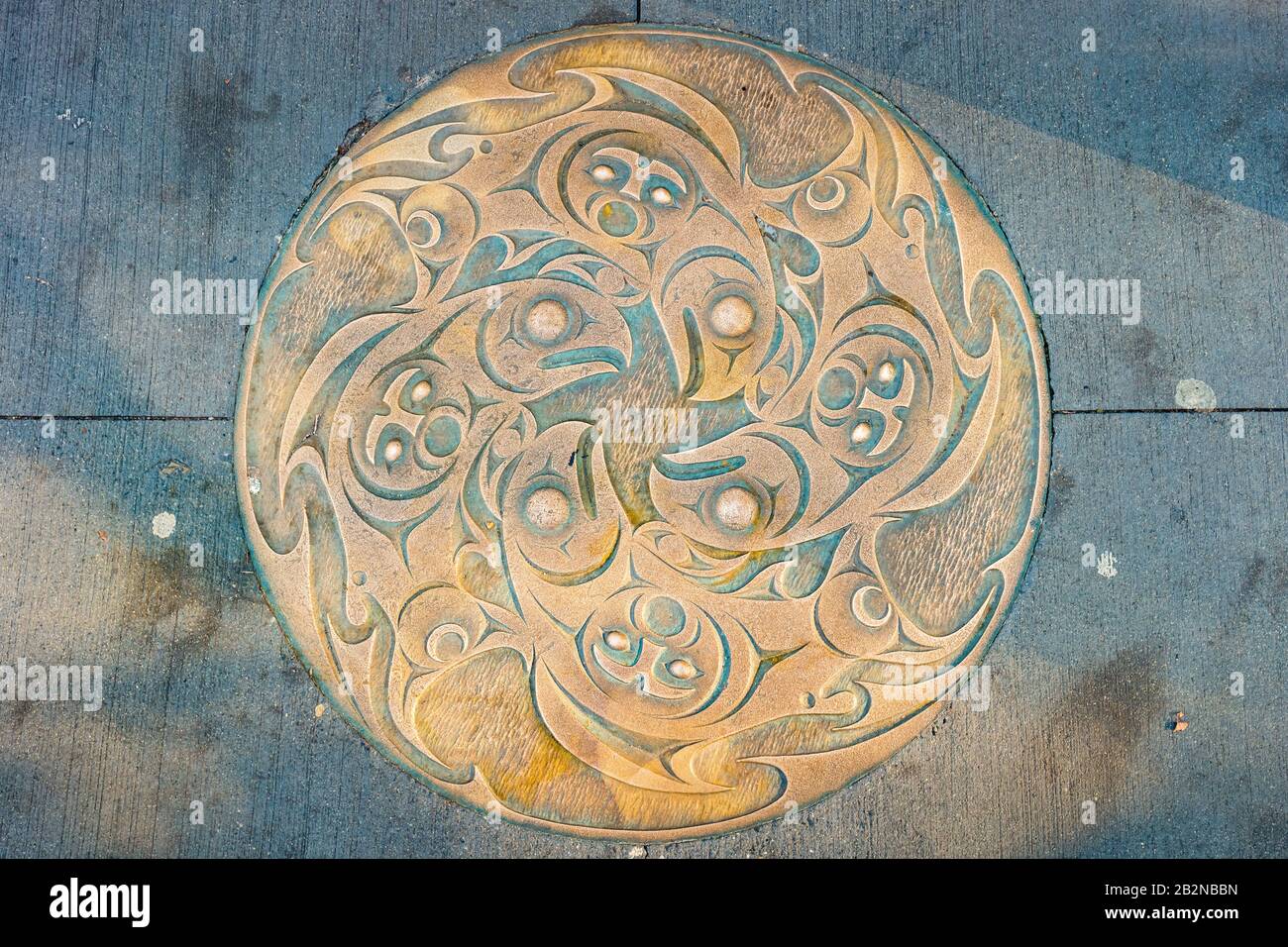 Verzierte Manhole-Abdeckung im Zentrum von Vancouver Canada, die sich mit dem Thema "First Nation" schmückt. Stockfoto
