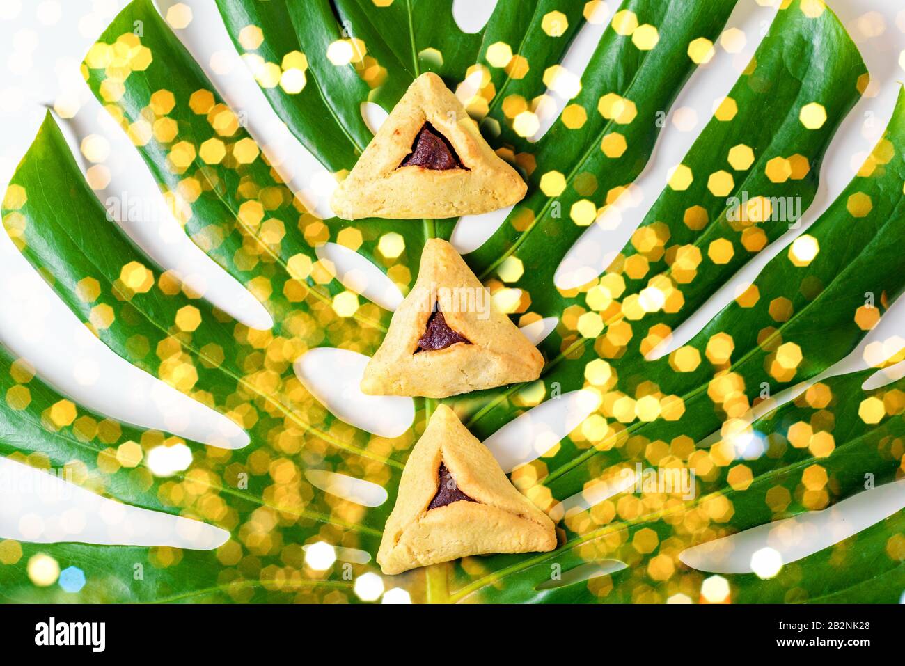 Gruppe von verschiedenen Dreieckskeksen Hamantaschen traditionelle Mahlzeit für den jüdischen Urlaub Purim auf Monstera-Blatt. Lamellen zur Schonung der Umwelt. Stockfoto
