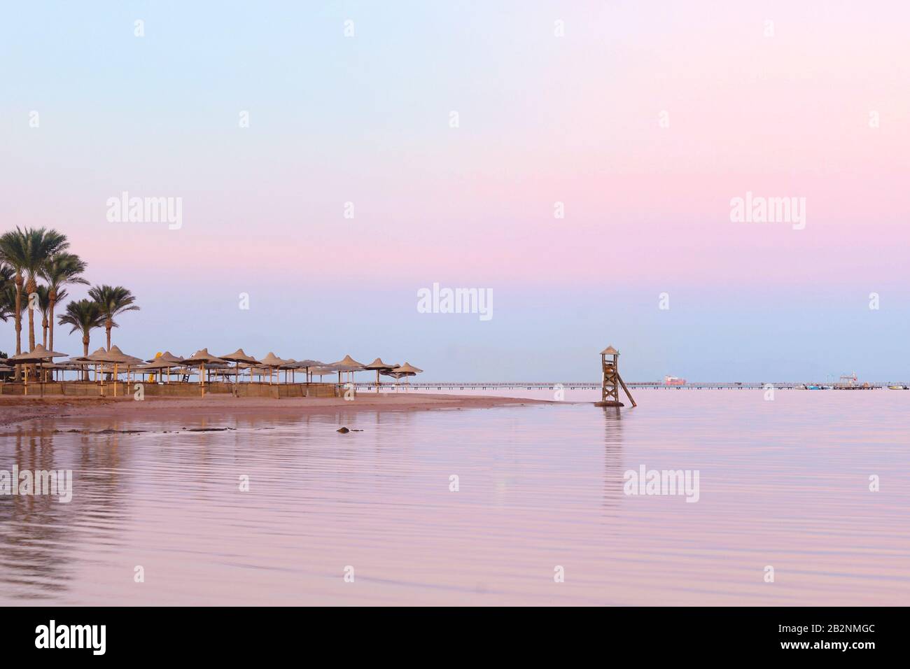 Leerer Strand bei rosafarbenem Sonnenuntergang in Ägypten. Blick auf den tropischen, leeren, sandigen Strand mit Sonnenschirmen und Strandbetten. Ruhiger Meerblick Stockfoto