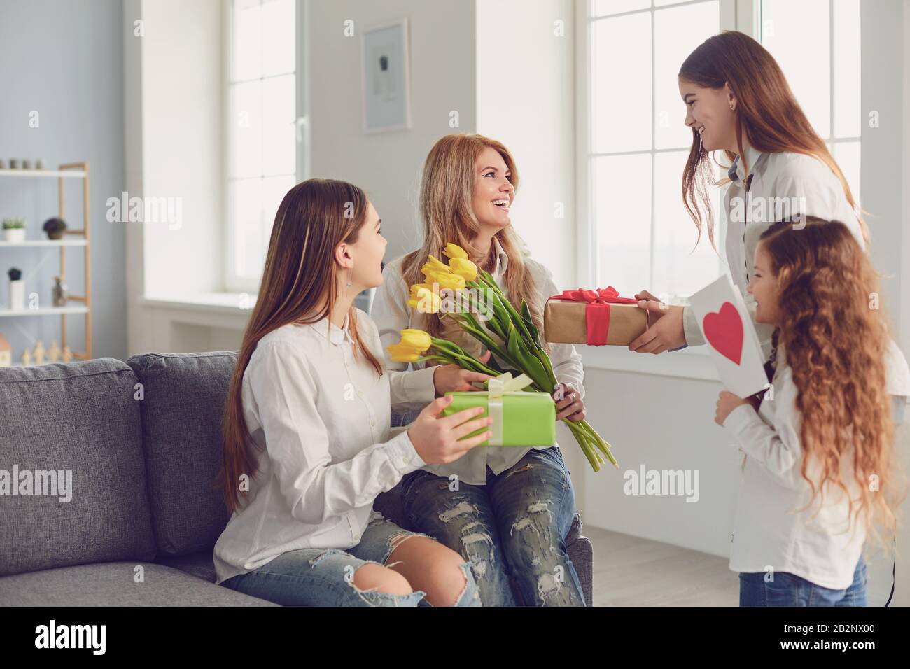 Froher Muttertag. Kindertöchter geben Mutter zu Hause einen Blumenstrauß. Stockfoto