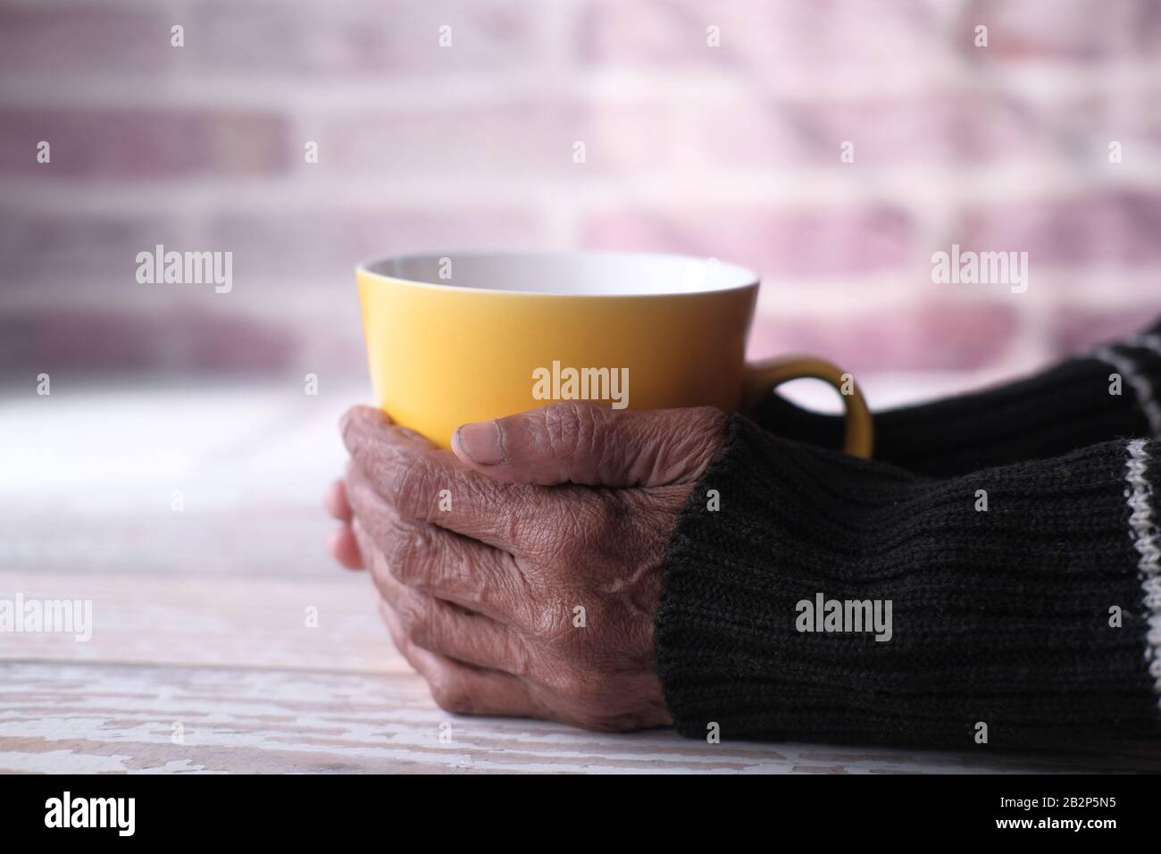 Eine ältere Frau, die eine Tasse Kaffee oder Tee in den Händen hält Stockfoto