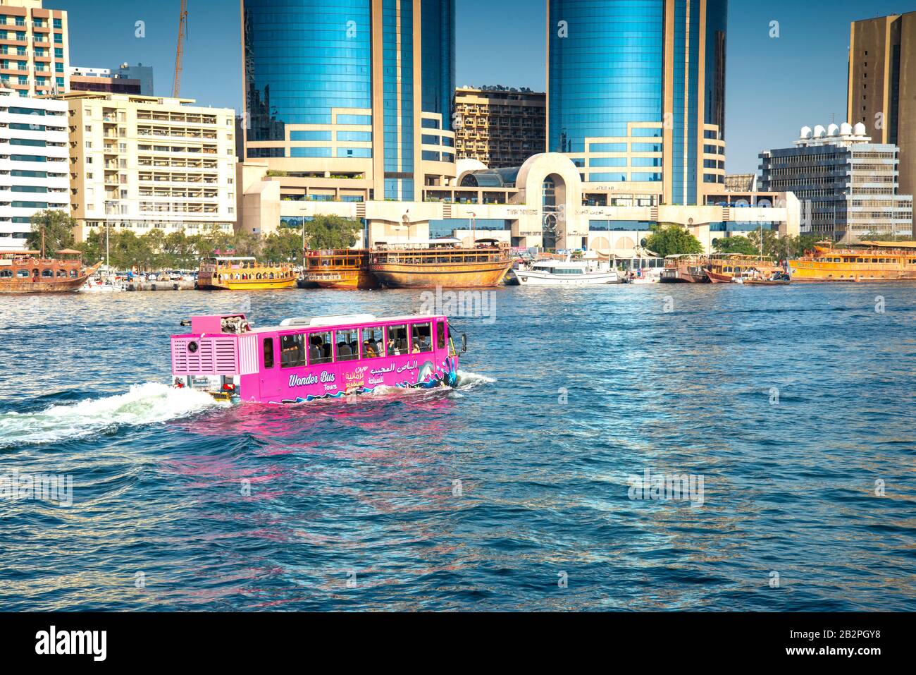 Amphibienfahrzeug rosa Wunder Tour Bus, so dass es entlang der Dubai Creek. Vor dem Hintergrund der modernen Dubai Waterfront Hotels, gesäumt mit Dhaufbooten. Stockfoto