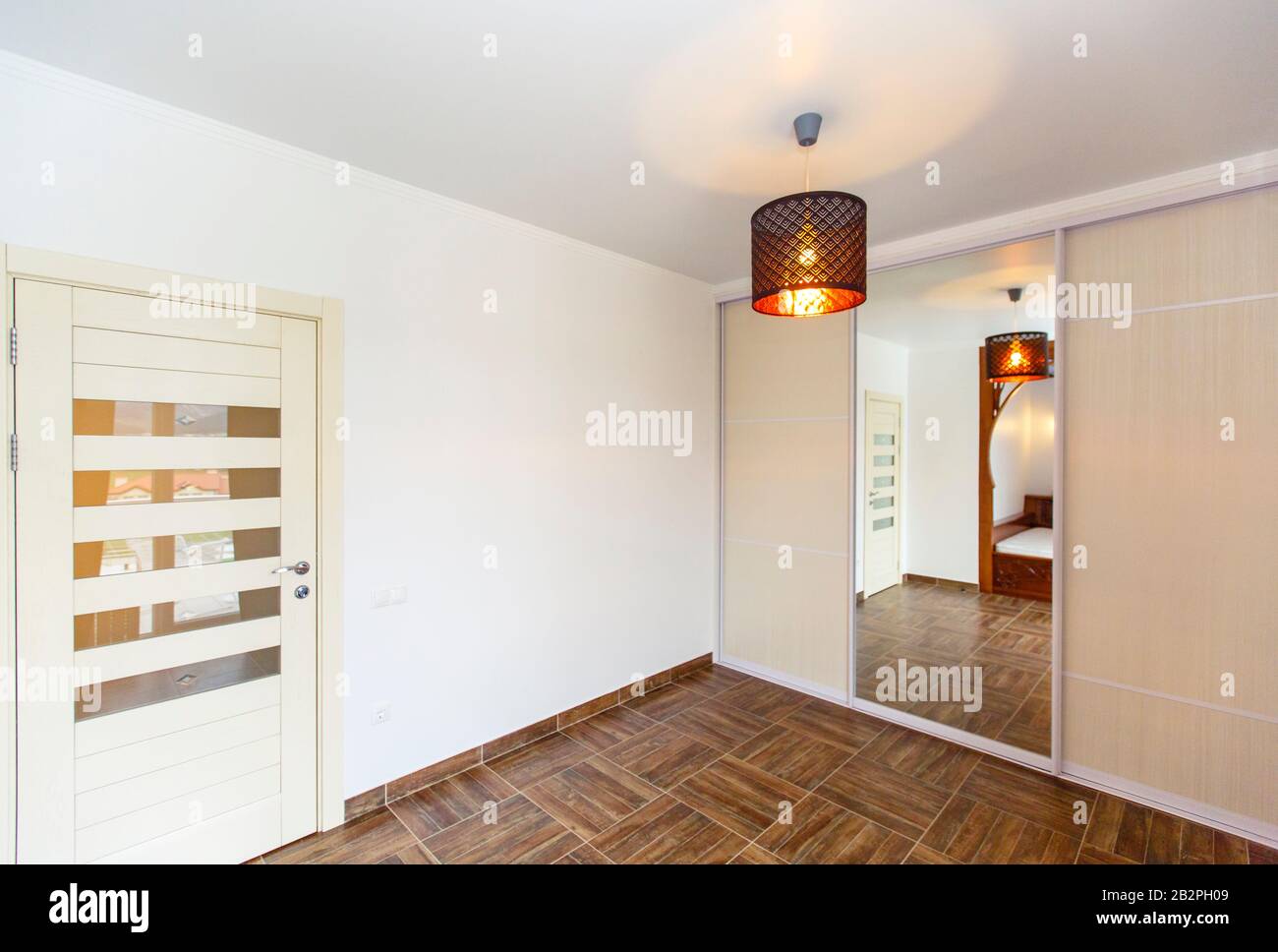 Ecke des Zimmers mit Spiegel im schrank, Tür, Kronleuchter und beigefarbenen Fliesen auf dem Boden. Stockfoto
