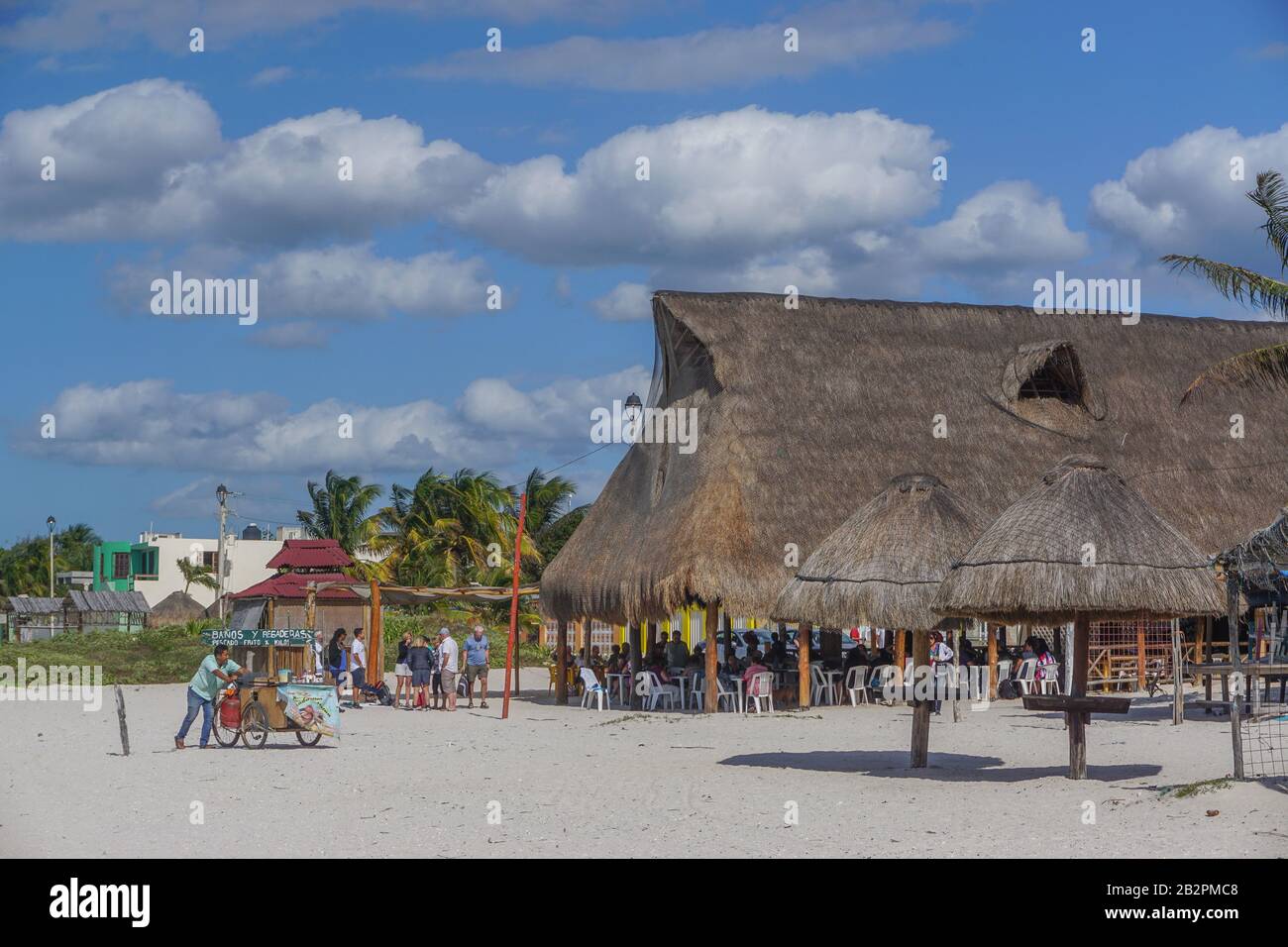 Celestun, Yucatan, Mexiko: Ein Händler treibt seinen Wagen an Kunden vorbei, die sich in einem Restaurant am Strand entspannen. Stockfoto