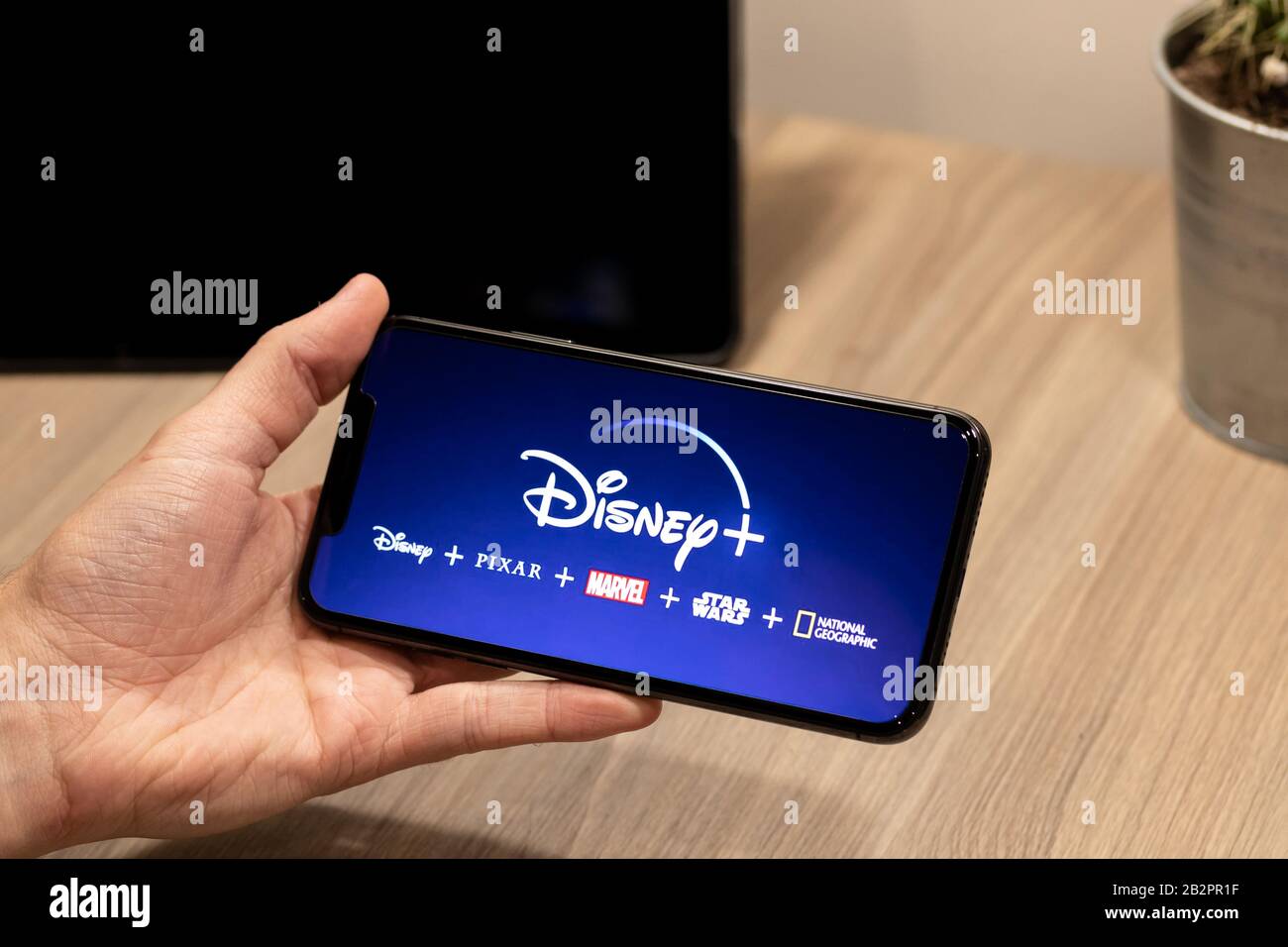 Mann auf einem Schreibtisch mit Blick auf Disney Plus (+) Streaming-Service-Logo mit Marken- / Kanal-Symbole unten. Stockfoto