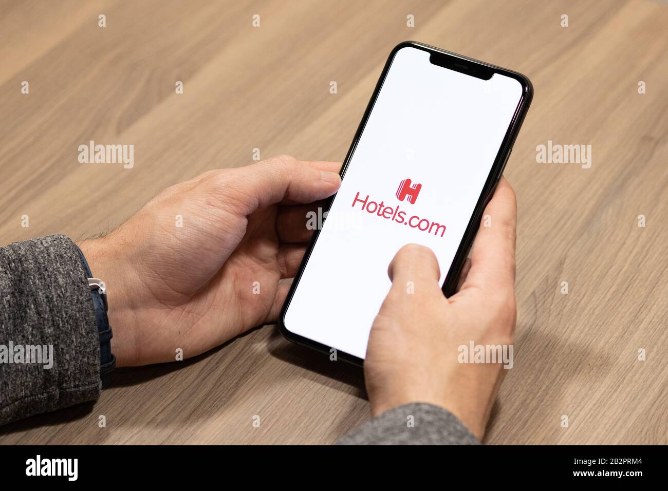 Mann, der ein iPhone am Schreibtisch verwendet, da das Hotels.com-Logo auf dem Bildschirm angezeigt wird. Stockfoto