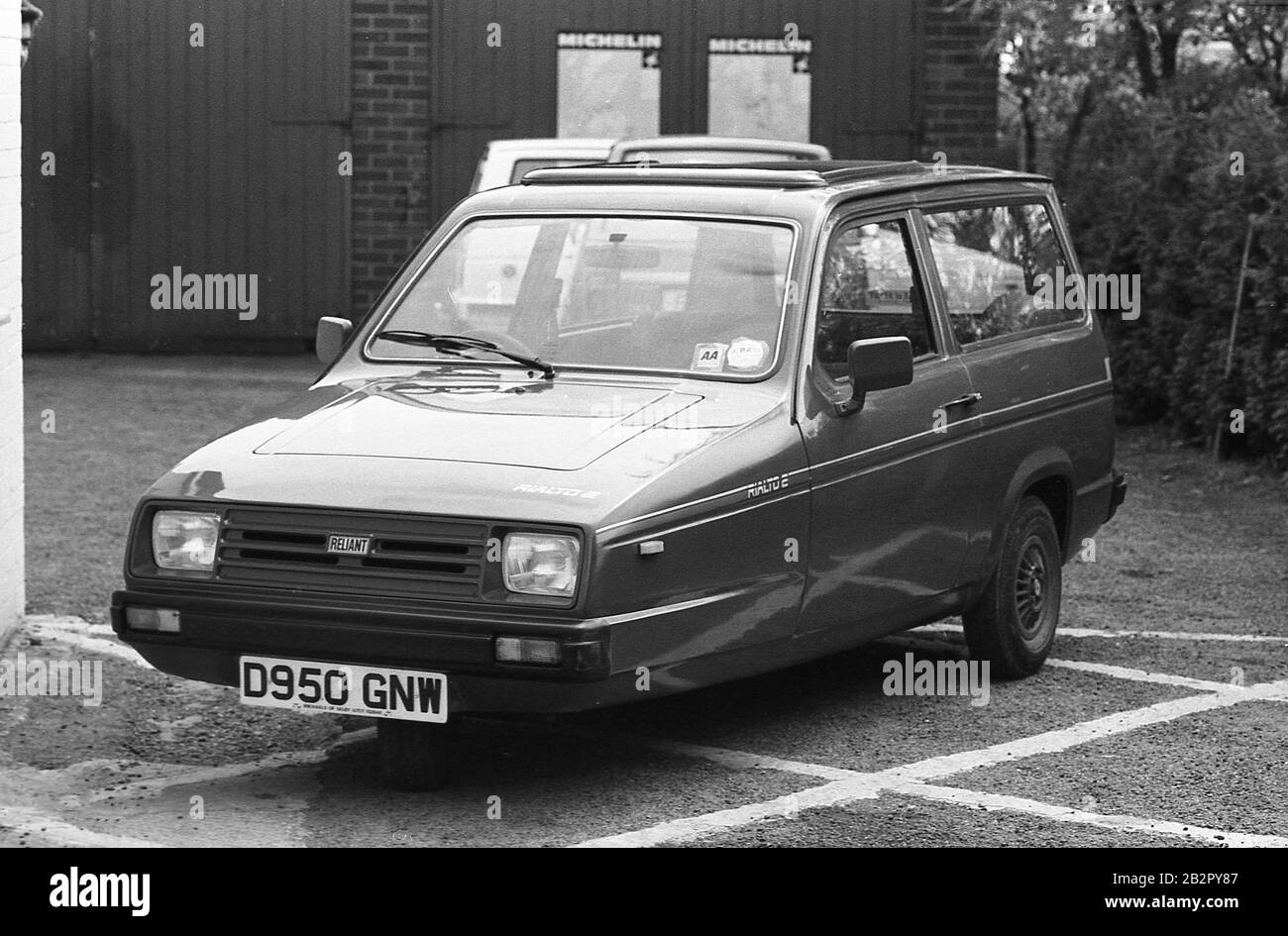 80er Jahre, historisch, ein Reliant Rialto 2-Kombi, der vor einigen Garagentüren abgestellt wurde. Der aus Fiberglas gebaute Dreiradwagen ersetzte den Reliant Robin und war die zweite Version des Rialto-Modells, das von 1983 bis 1986 produziert wurde. Stockfoto