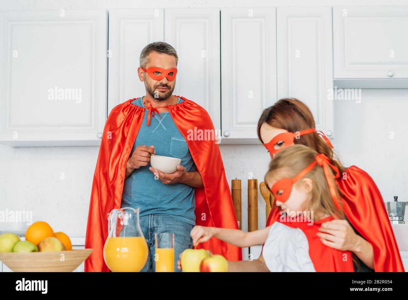 Vater, Mutter und Tochter in Kostümen von Superhelden, die in der Küche frühstücken Stockfoto