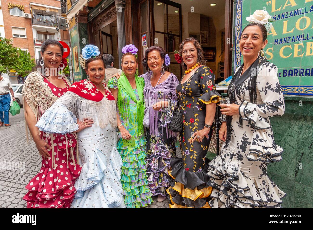 Eine Gruppe von Frauen, die während der Aprilmesse in Sevilla, Spanien, bunte Flamenco-Kleider vor einer Bar tragen Stockfoto