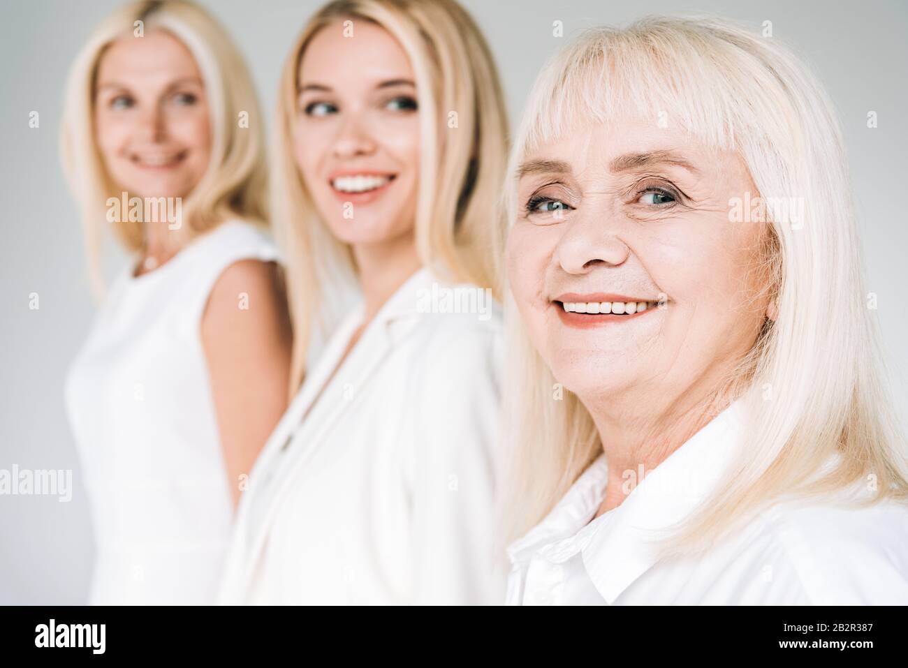 Selektiver Fokus der drei Generationen blonden Frauen isoliert auf Grau Stockfoto