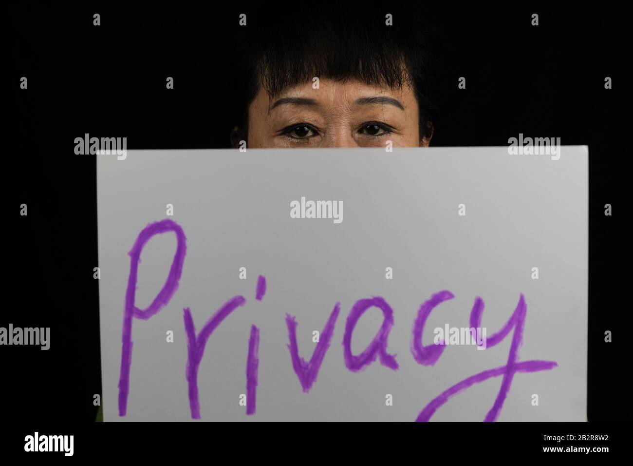 Frau bedeckt ihr Gesicht mit einem Papier mit einer Privatsphäre Text darauf vor schwarzem Hintergrund geschrieben Stockfoto