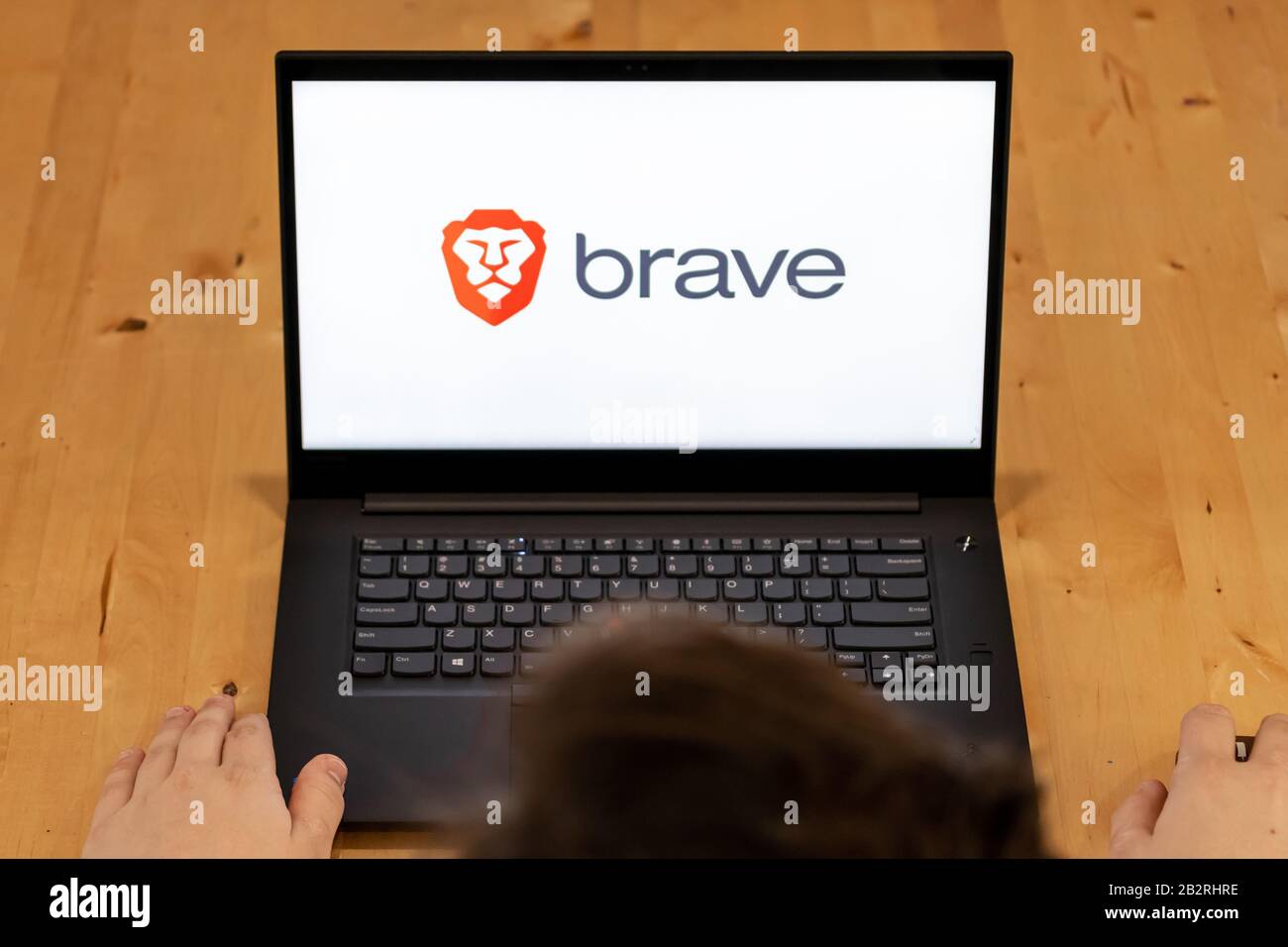 Ansicht von oben auf einen Mann, der an einem Schreibtisch sitzt und einen Laptop mit dem Brave Browser-Logo auf dem Bildschirm verwendet. Stockfoto