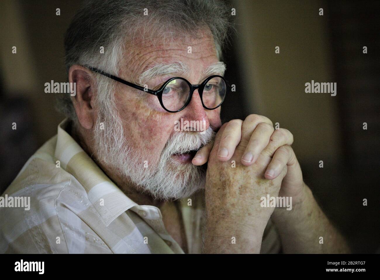 Älterer richtiger Mann mit runder Brille und grauem Bartdenken mit gekleppten Händen Schriftsteller Fotograf Philosoph Vater Großvater Stockfoto