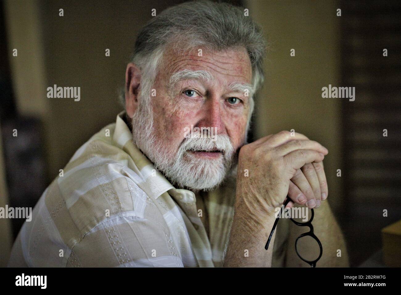 Älterer richtiger Mann mit runder Brille und grauem Bartdenken mit gekleppten Händen Schriftsteller Fotograf Philosoph Vater Großvater Stockfoto