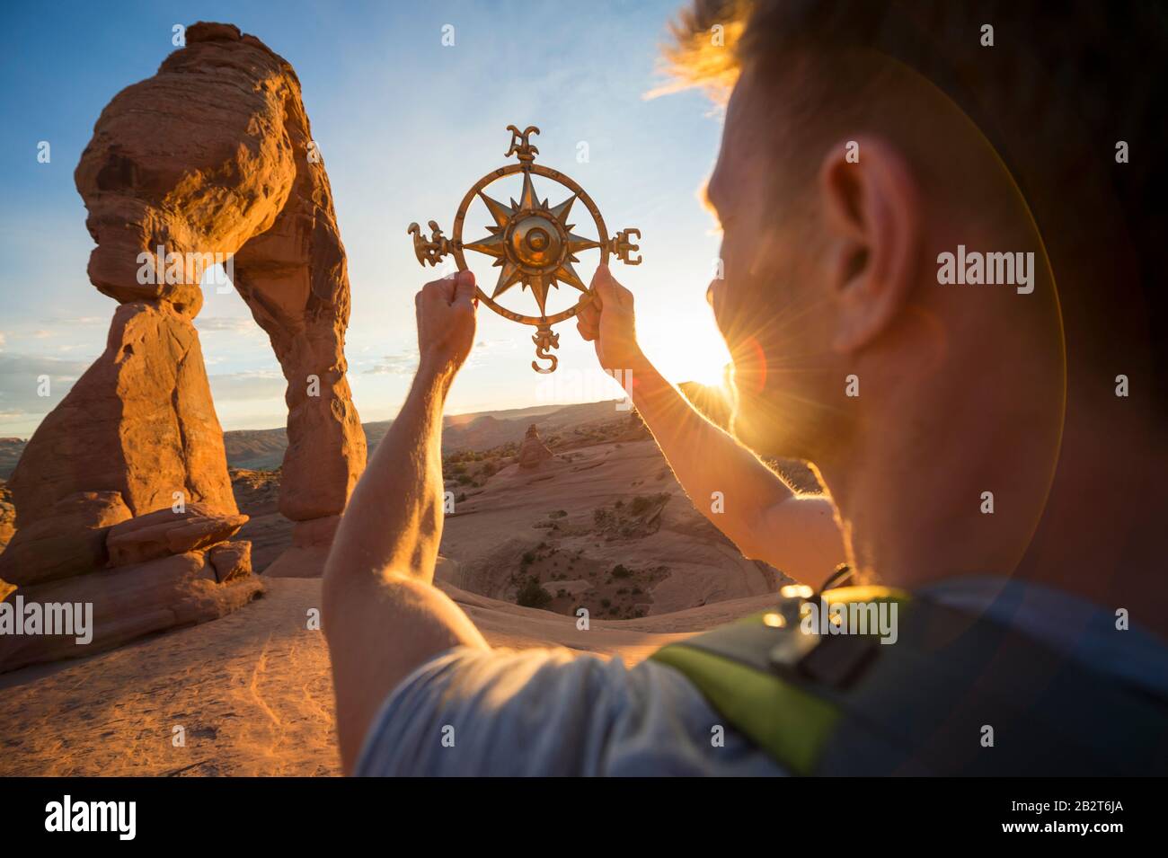 Backpacker, der traditionellen Kompass hält, erhob sich vor goldenem Sonnenuntergang bei dramatischem Steinbogen Stockfoto