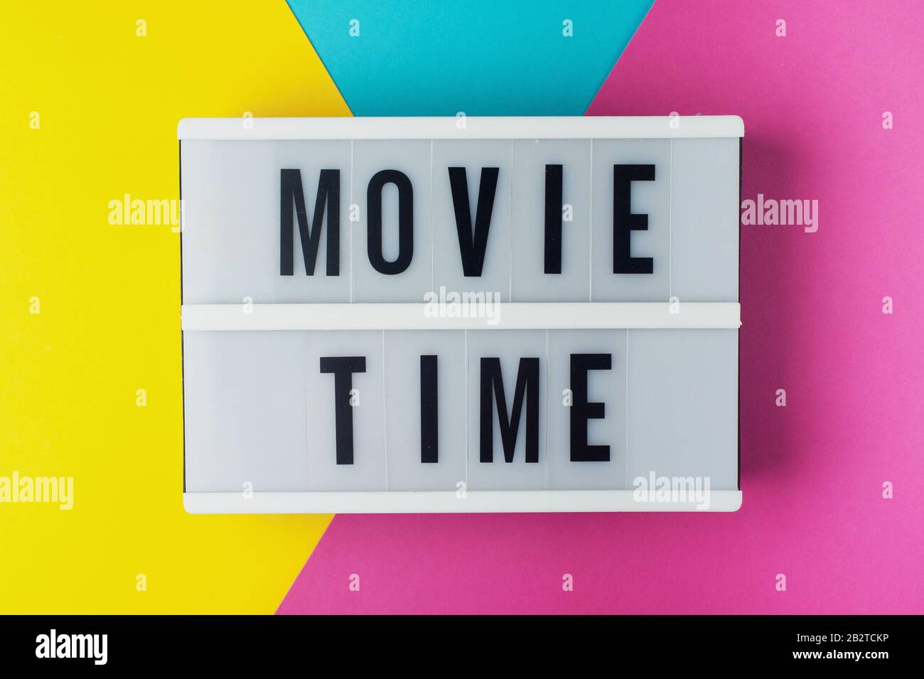 Filmzeit: Text in einem Leuchtkasten auf blauem, gelbem und rosafarbenem Hintergrund. Stockfoto